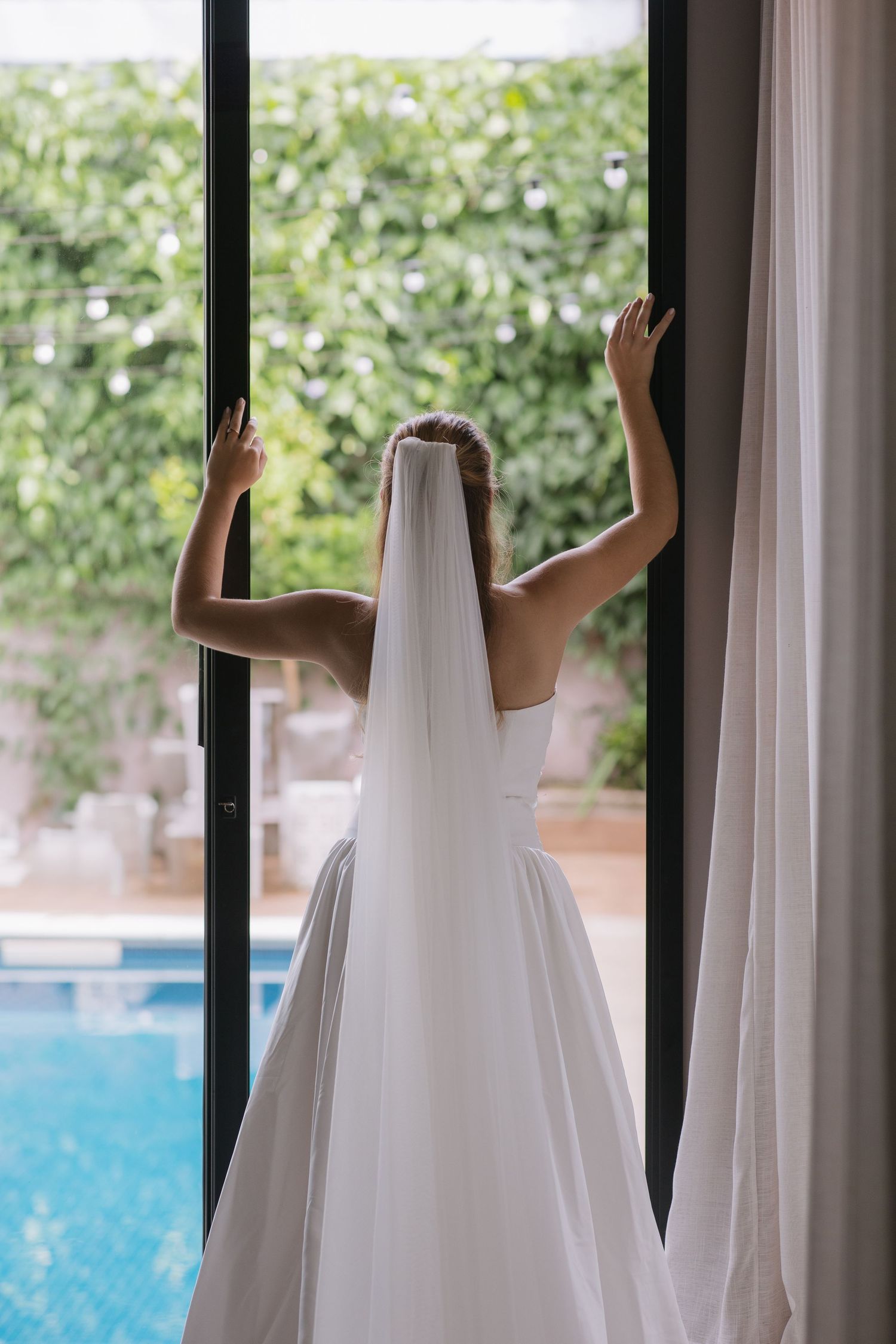 White towels hanging on black metal rods against a window overlooking a swimming pool.
