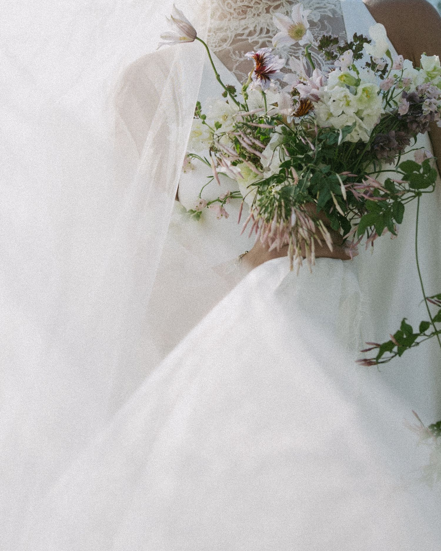 Elegant white wedding dress detail with delicate floral bouquet arrangement.
