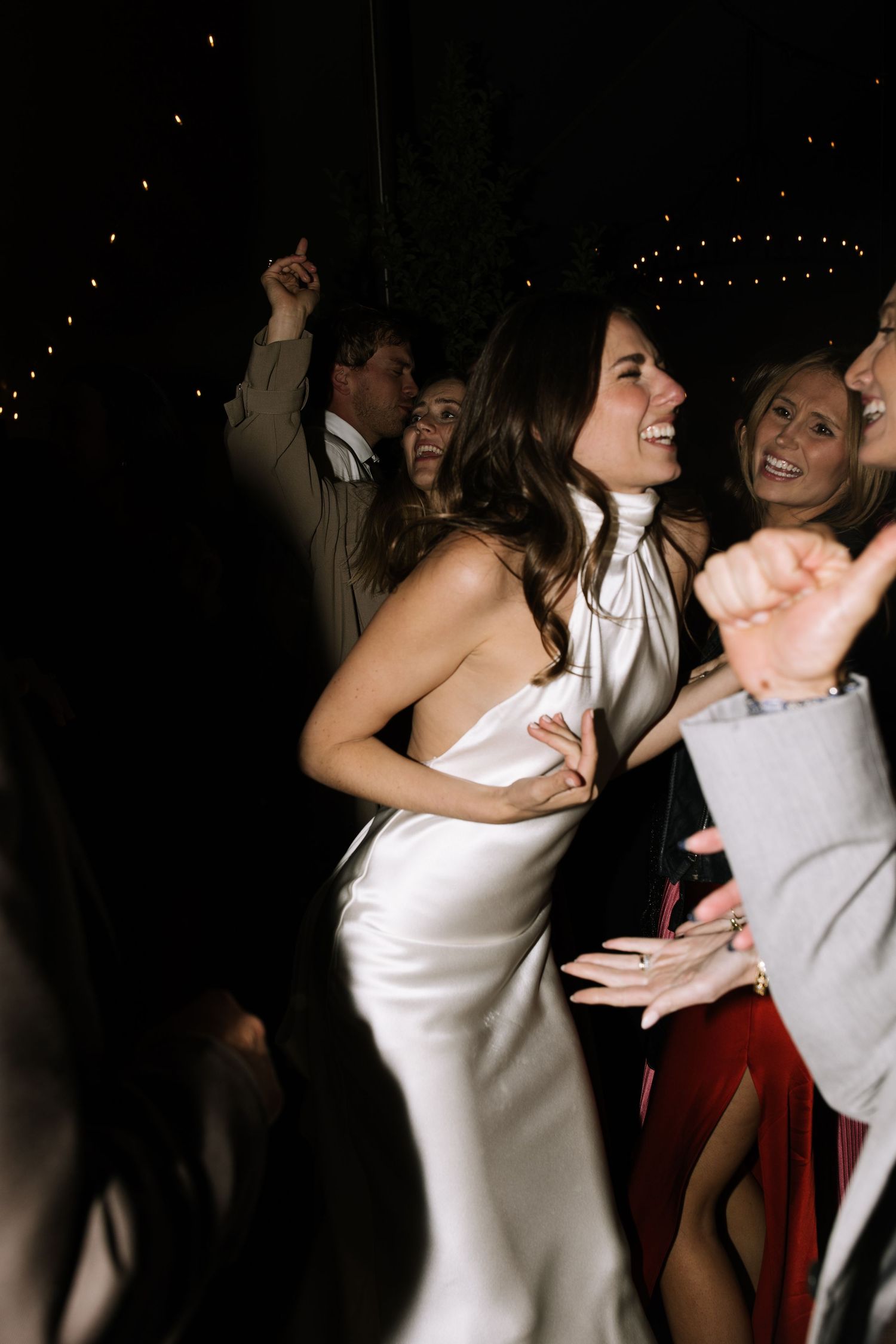 Couples dancing energetically at a dark reception venue with string lights overhead.