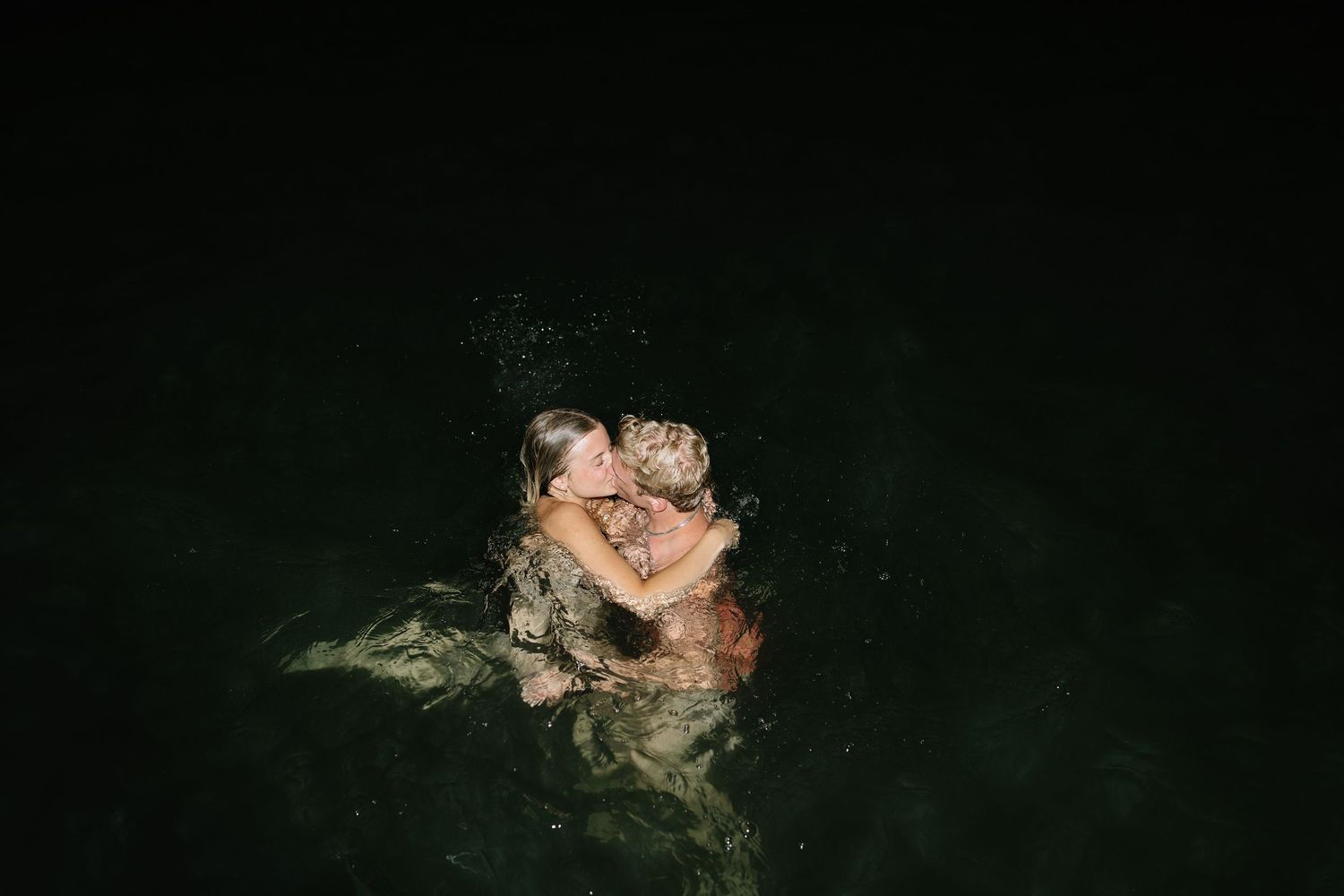 Intimate nighttime swimming scene with dark water and reflections.