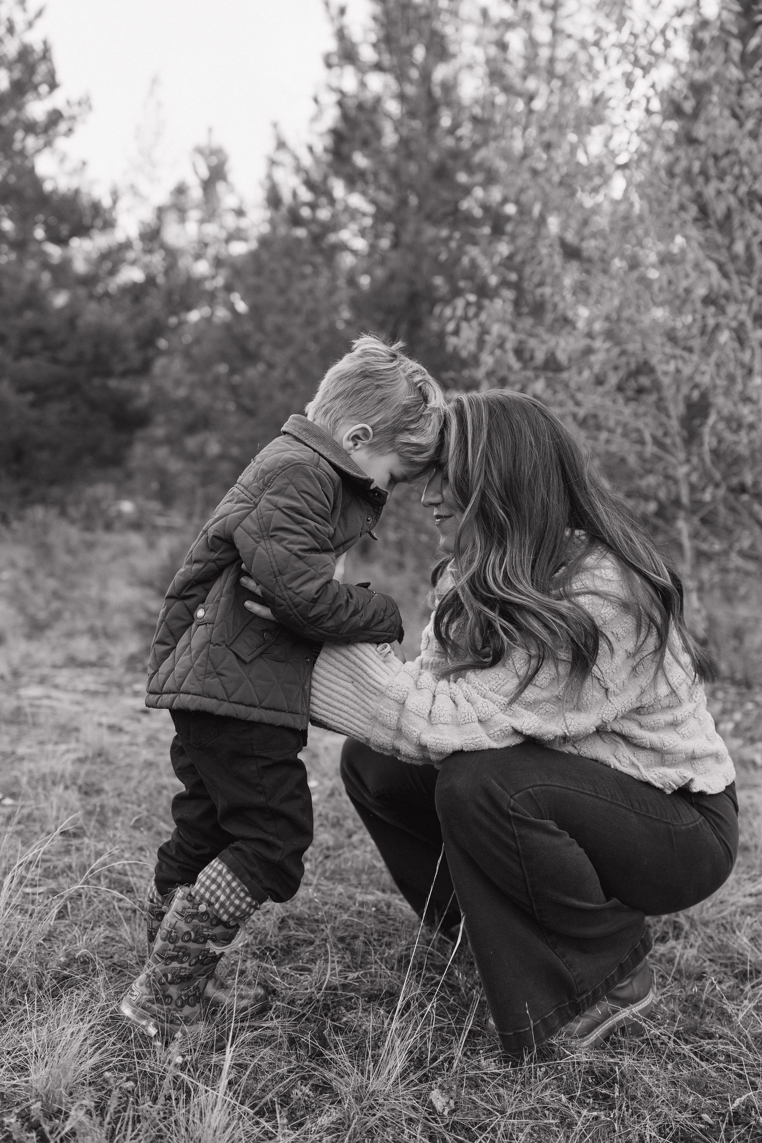 Black and white outdoor family moment captured among pine trees.