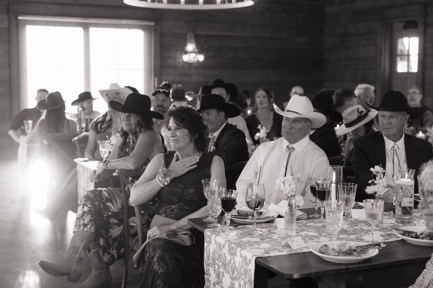 Black and white photo of guests in cowboy hats seated at tables during a western-themed wedding reception.