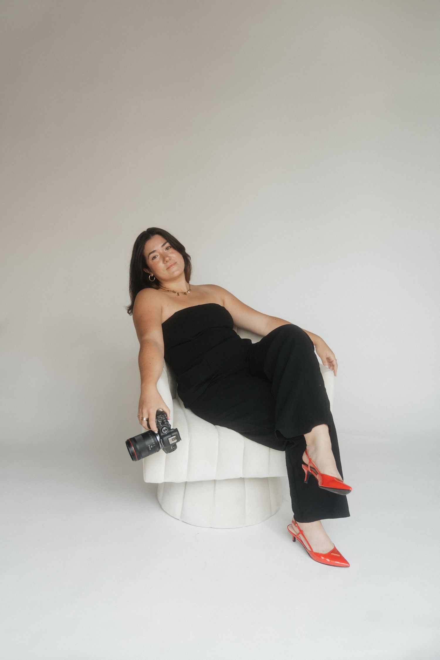Woman in black dress lounges artistically on white modern furniture with red heels.