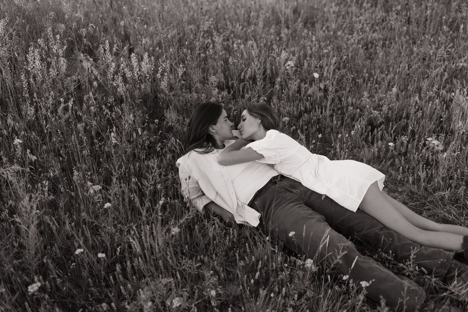 Couple lying together in tall grass during golden hour.