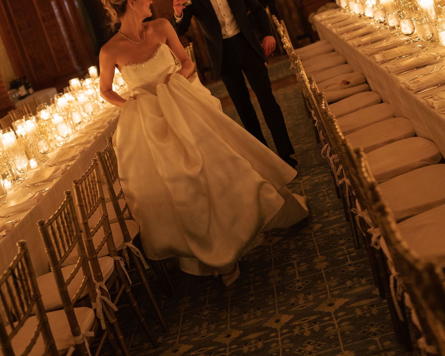Wedding dress silhouette glides past candlelit reception tables.