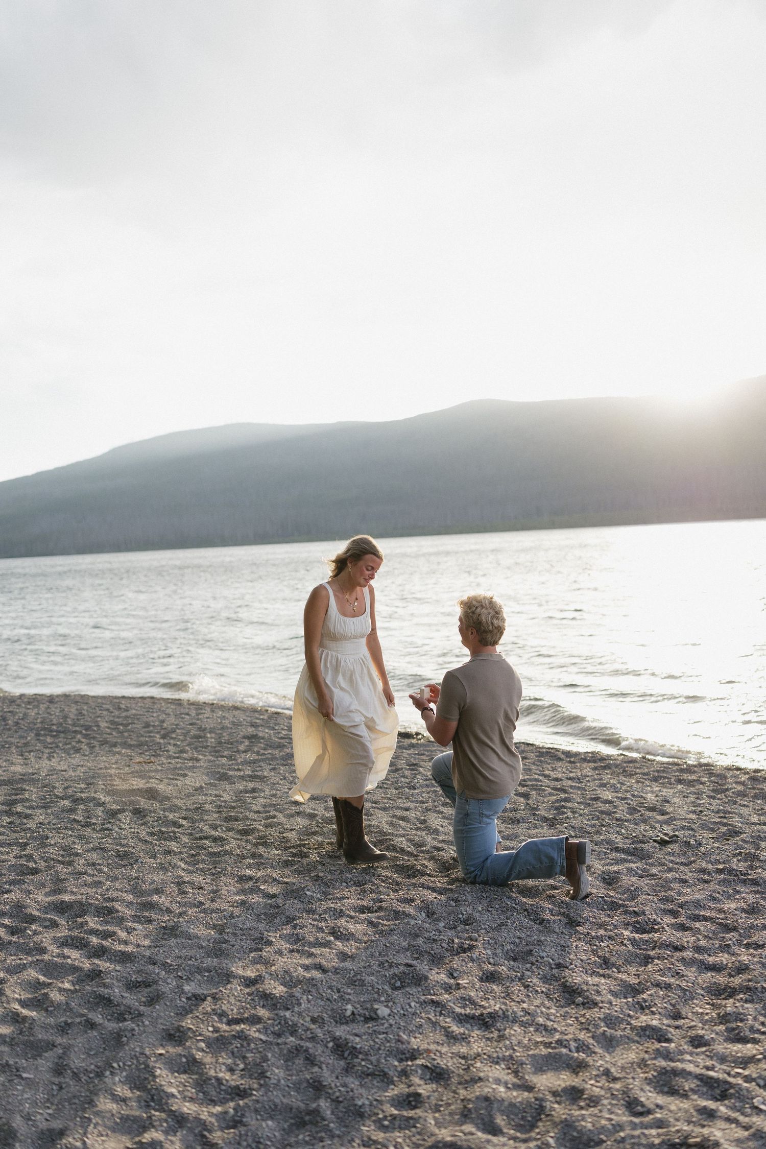 A proposal scene on a beach at sunset with mountains in the background.