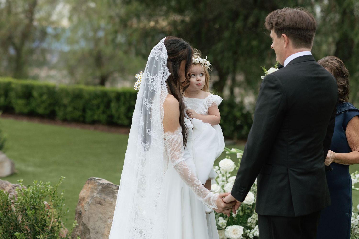 Outdoor garden wedding ceremony with flowing veil and floral arrangements.