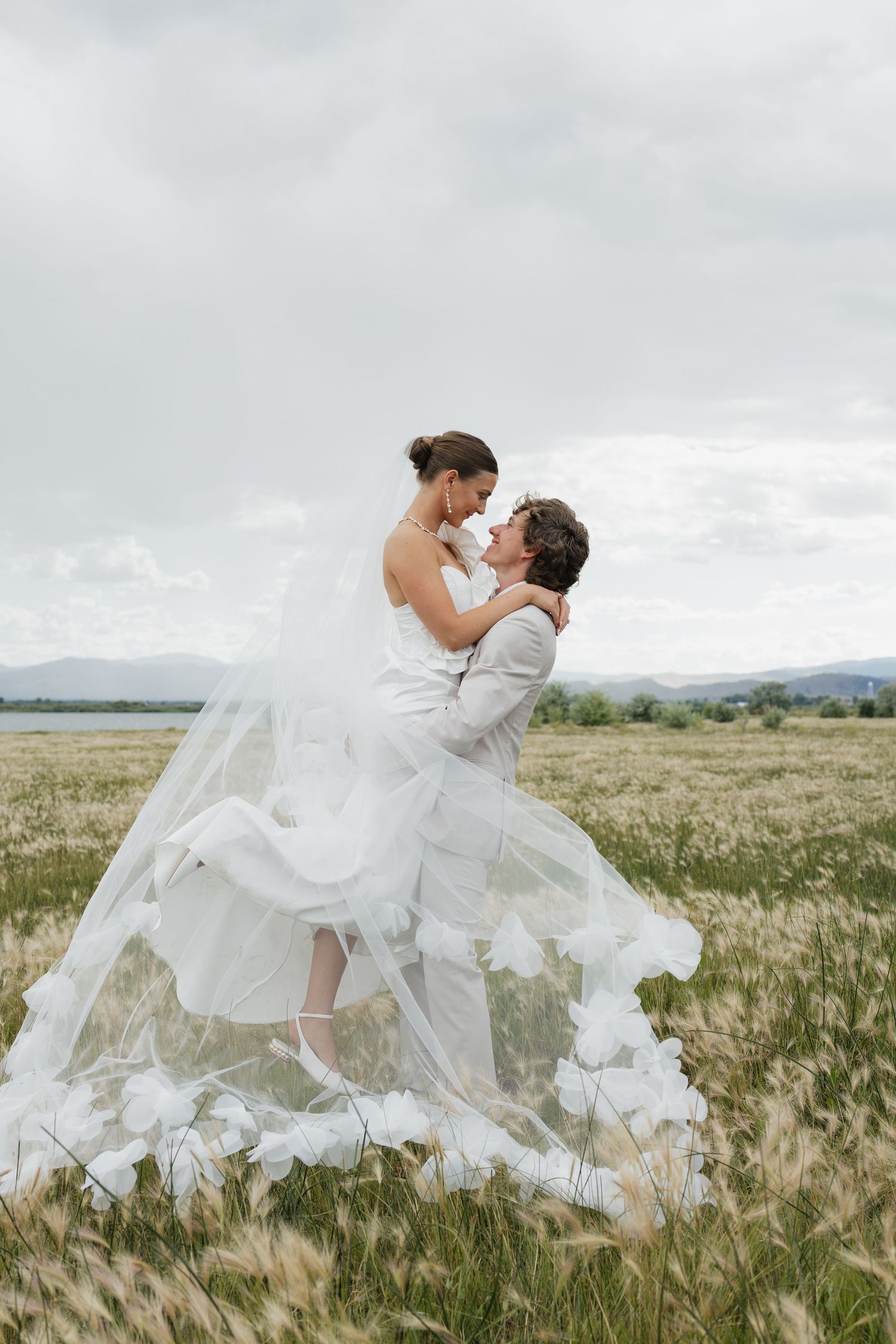 Romantic wedding couple embraces in a dramatic lift pose against a scenic mountain backdrop.
