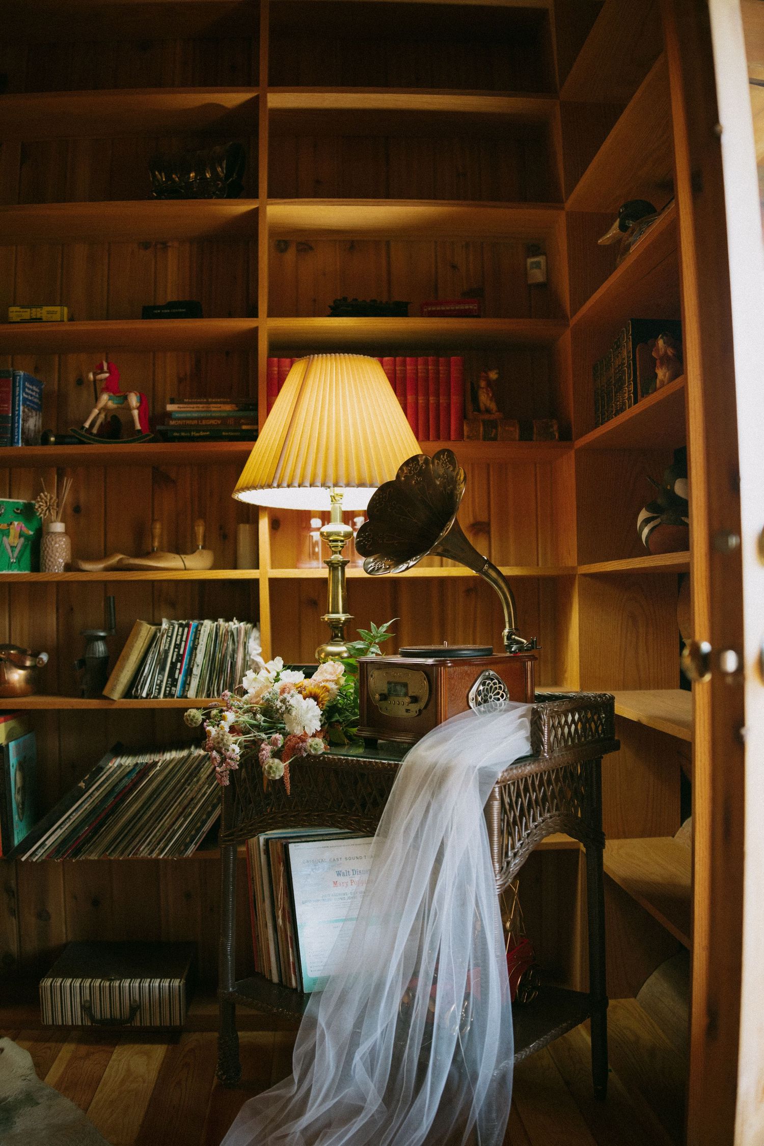 Cozy library interior with wooden shelves, warm lamp lighting, and a white draped fabric creating an intimate atmosphere.