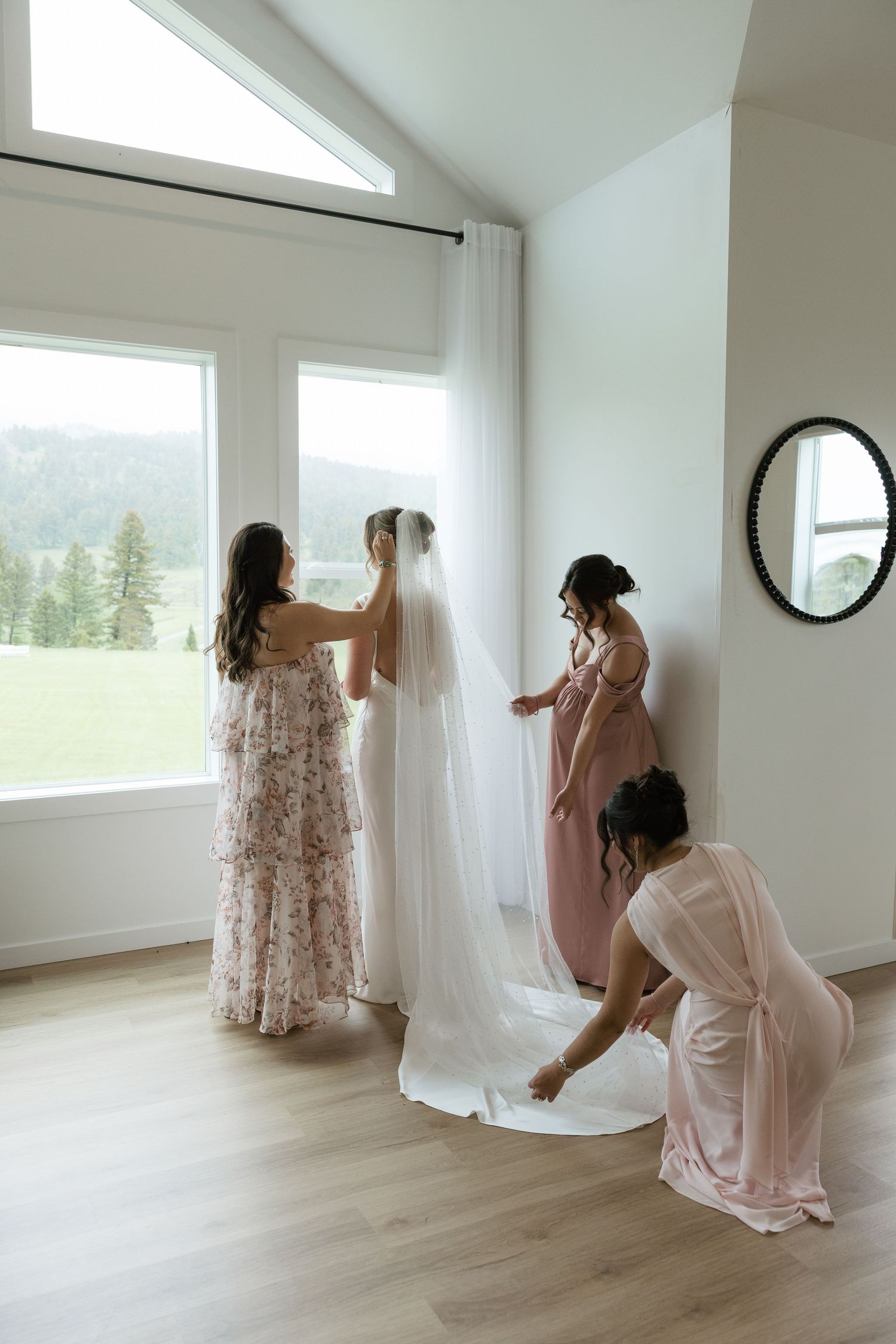 Bridesmaids helping bride with veil and dress in bright white room before wedding ceremony.