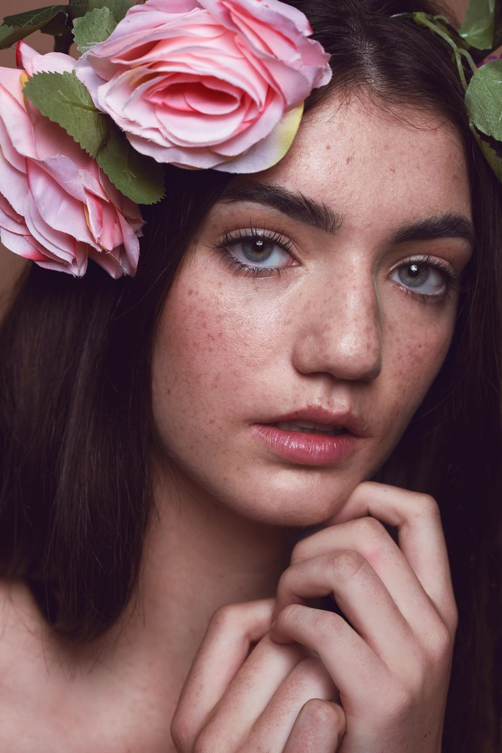 A photo of a woman taken by Jr Francisco with freckles and gray eyes wearing pink roses flower crown, posing gracefully with hand near chin.
