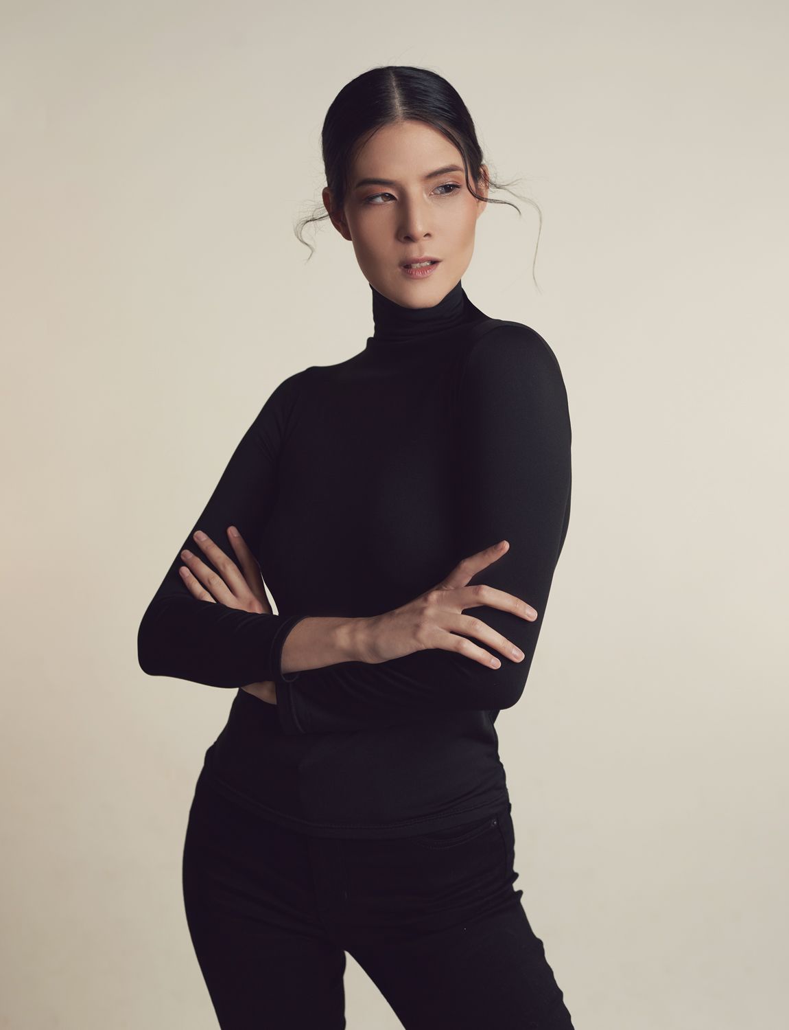 a photo Young  Woman taken by Jr Francisco in black turtleneck and pants, arms crossed, posing confidently against a neutral background.