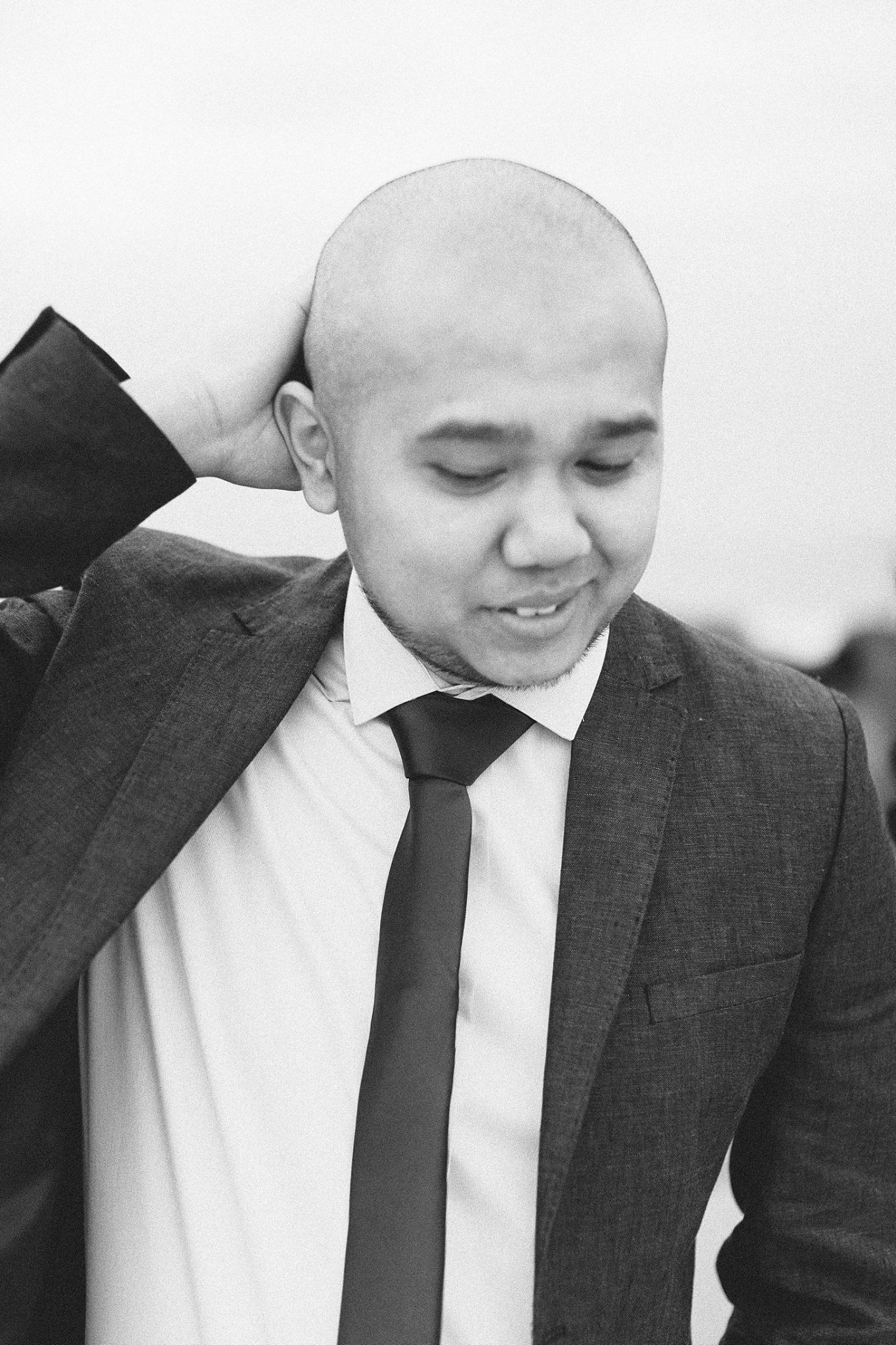 Black and white portrait of Orange County portrait photographer, Jr Francisco in a suit and tie, smiling with hand behind his head.