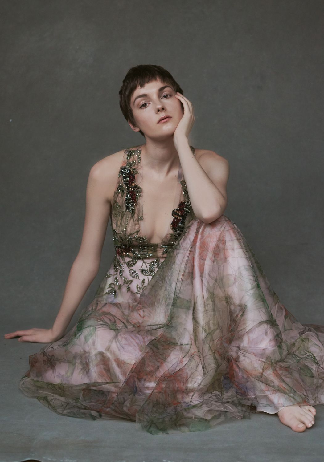 a photo Woman taken by Jr Francisco in floral embroidered green and pink sheer gown sits gracefully on floor against gray backdrop.