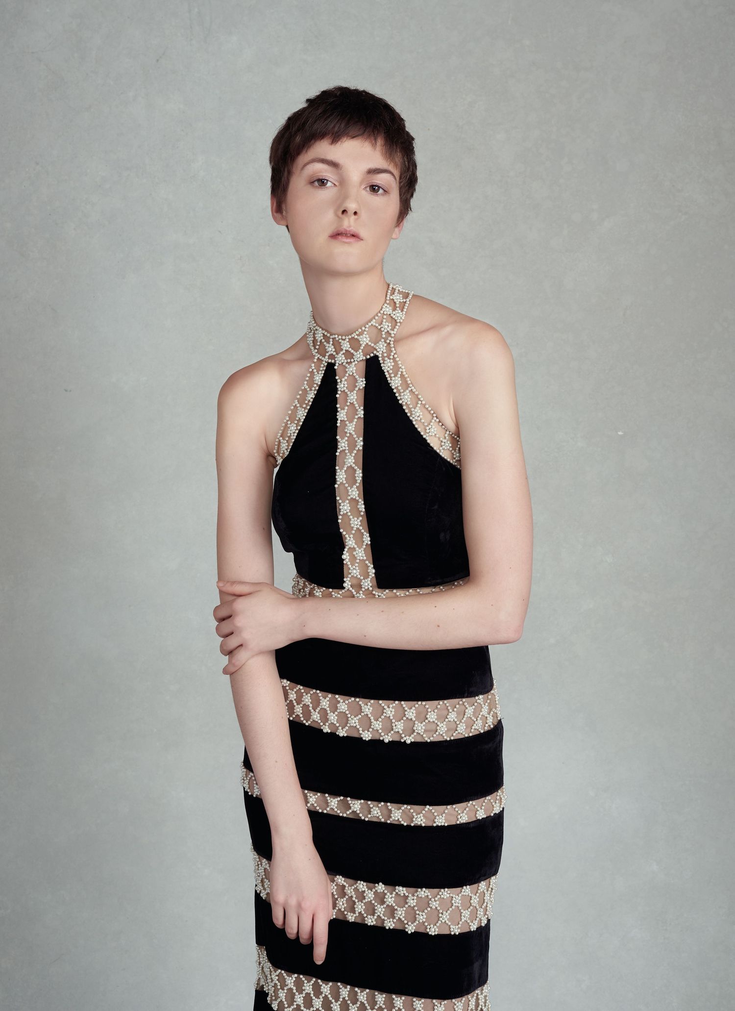 a photo by Jr Francisco of a Woman in black halter dress with gold lace trim and striped skirt, posing against gray background.