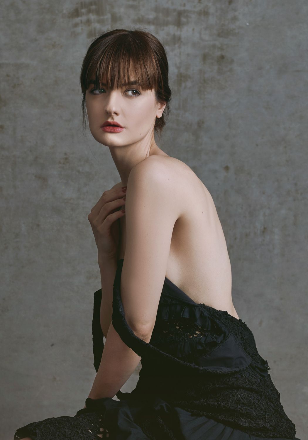 Portrait of a Young woman by Jr Francisco in a backless black gown poses gracefully with bangs and red lips against a gray backdrop.