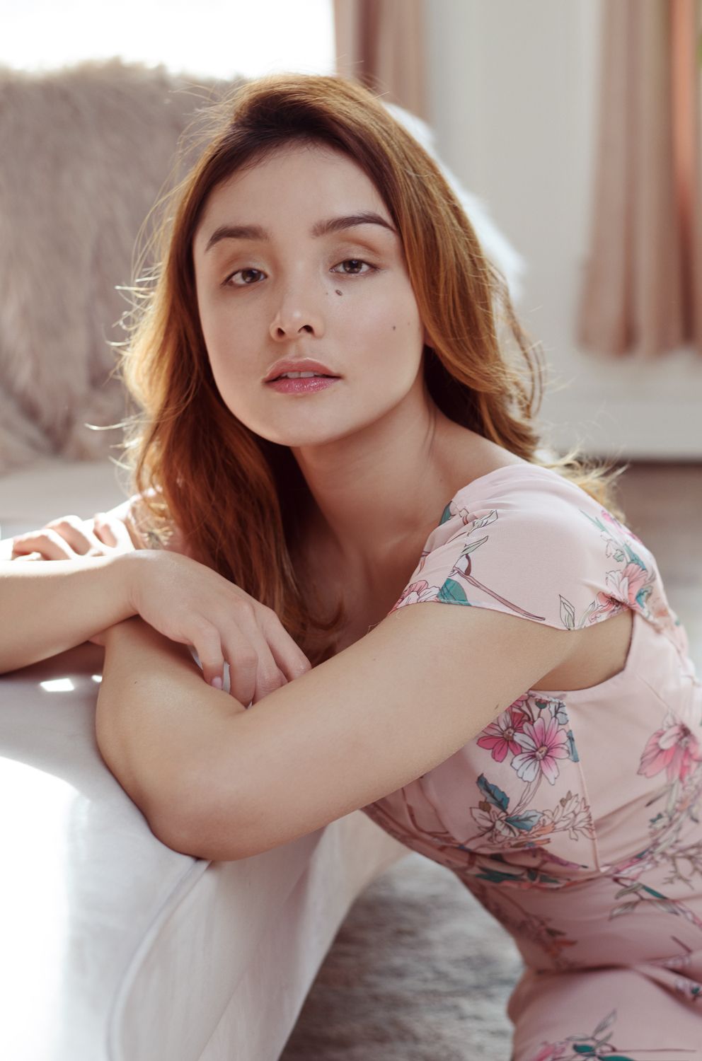 photo of Young woman by Jr Francisco with auburn hair in a pink floral off-shoulder dress sits gracefully on the floor in a bright room.
