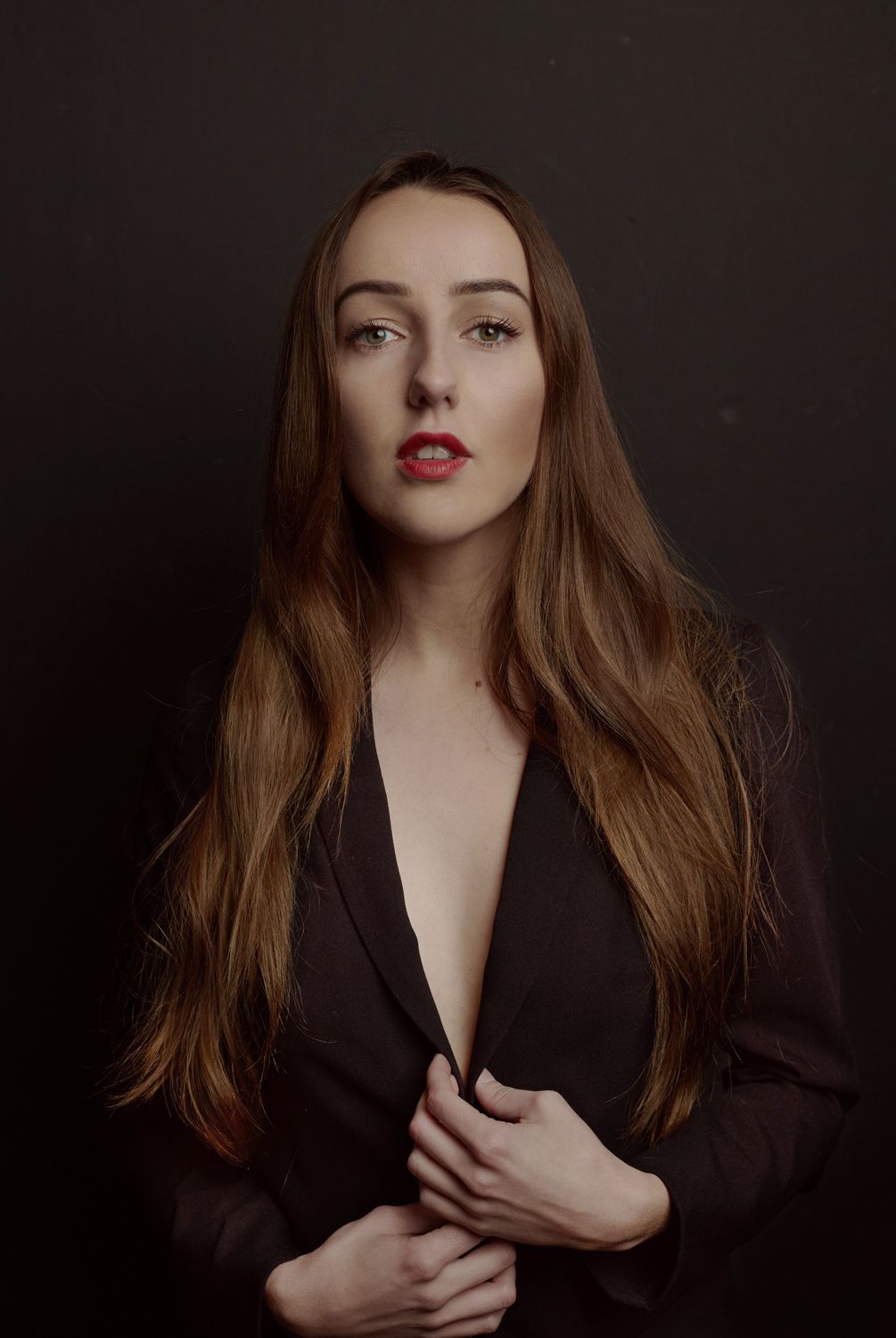 Photo of a Young woman by Jr Francisco with long hair and red lips wearing a black blazer, posing confidently against a dark background