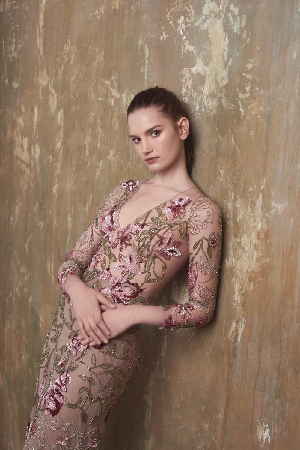 photo of Young woman by Jr Francisco in a floral embroidered sheer pink gown poses elegantly against a textured gold wall.