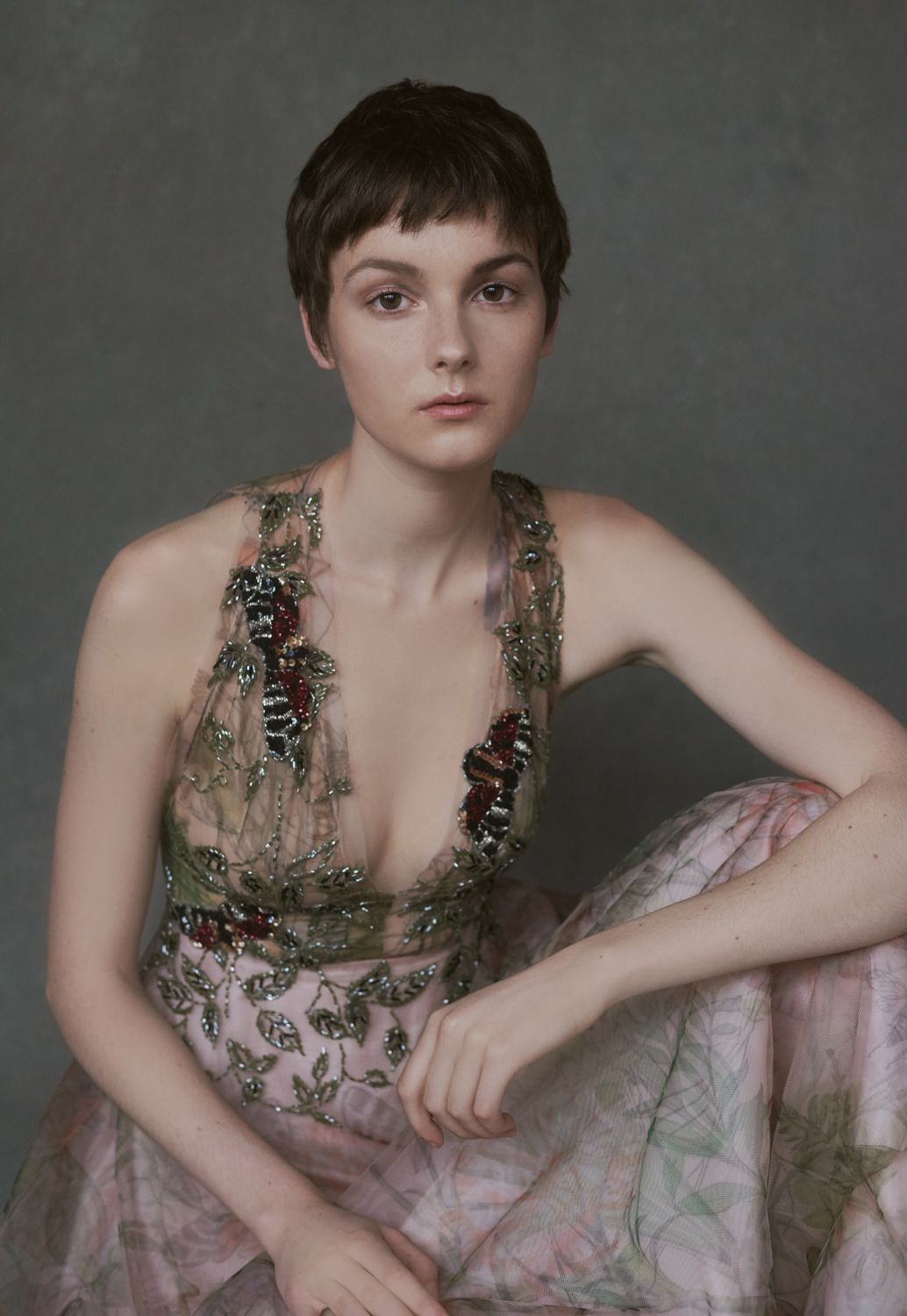 A photo of a Young woman taken by Jr Francisco with short dark hair wearing an sheer floral gown, seated gracefully in a gray background.
