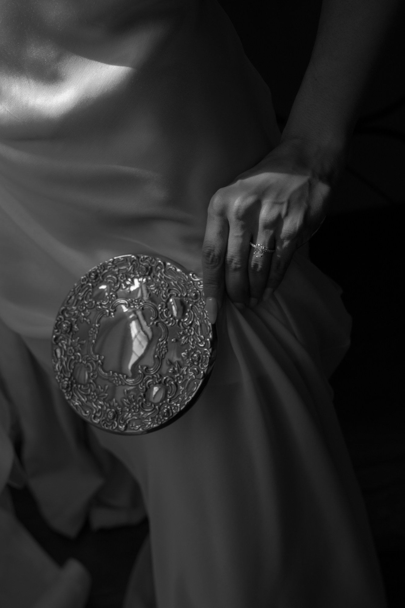 Black and white close-up of a bride holding an ornate silver clutch against her satin wedding gown.