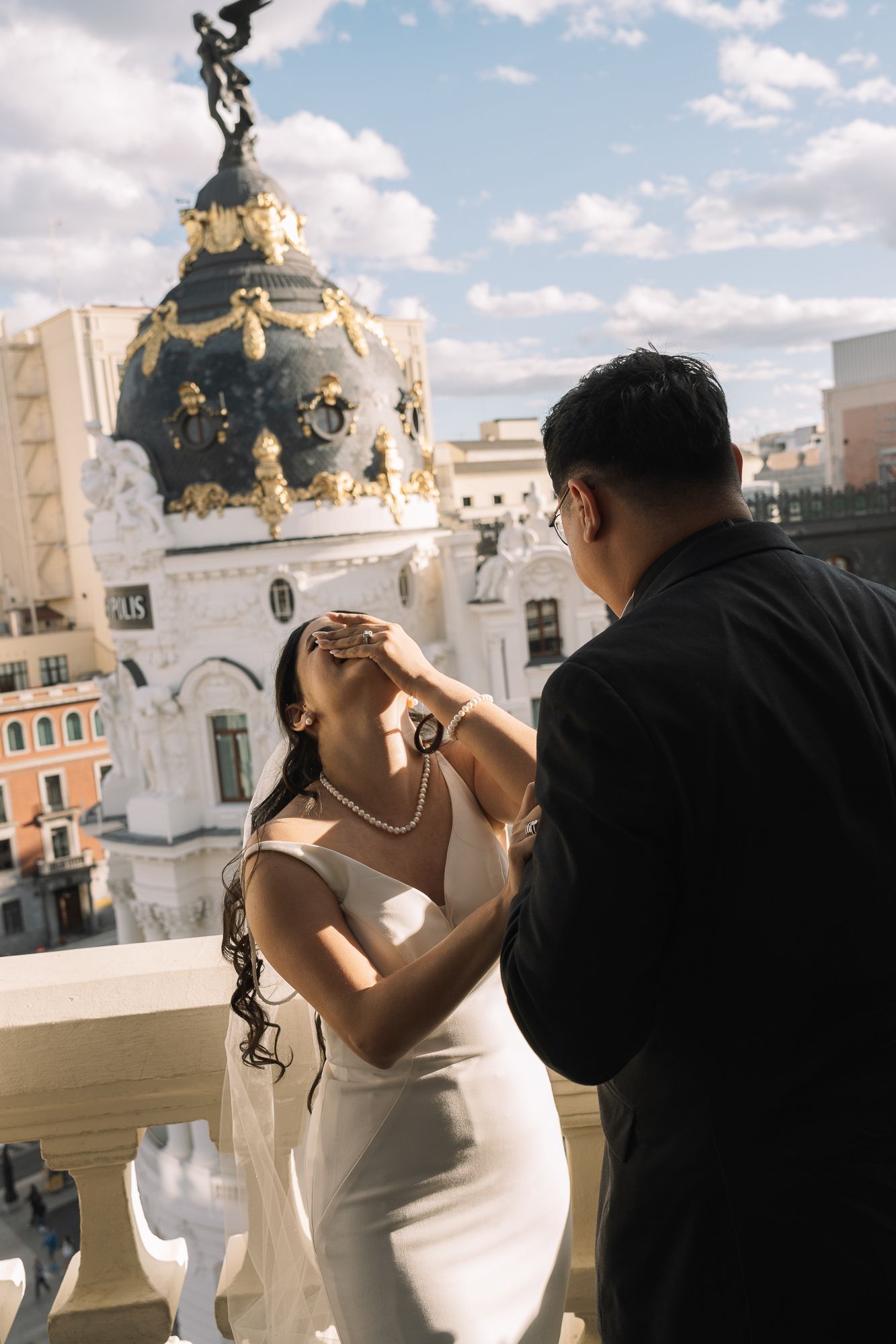 Couple shares a romantic moment on a rooftop terrace with ornate Metropolis building dome visible in Madrid skyline.