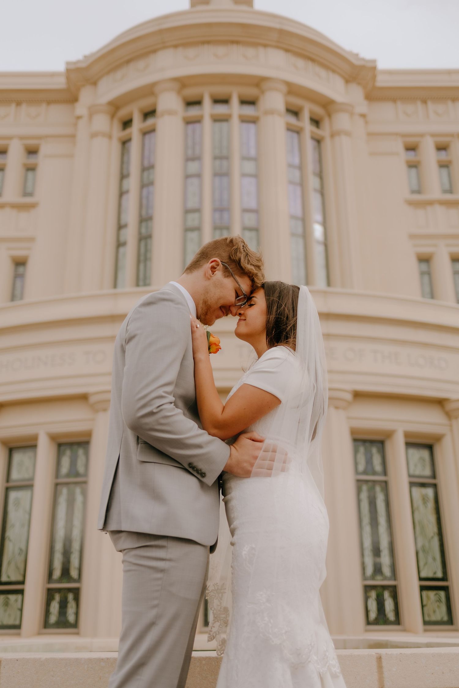 Bride and groom sharing an intimate moment, touching foreheads in front of a grand architectural building.