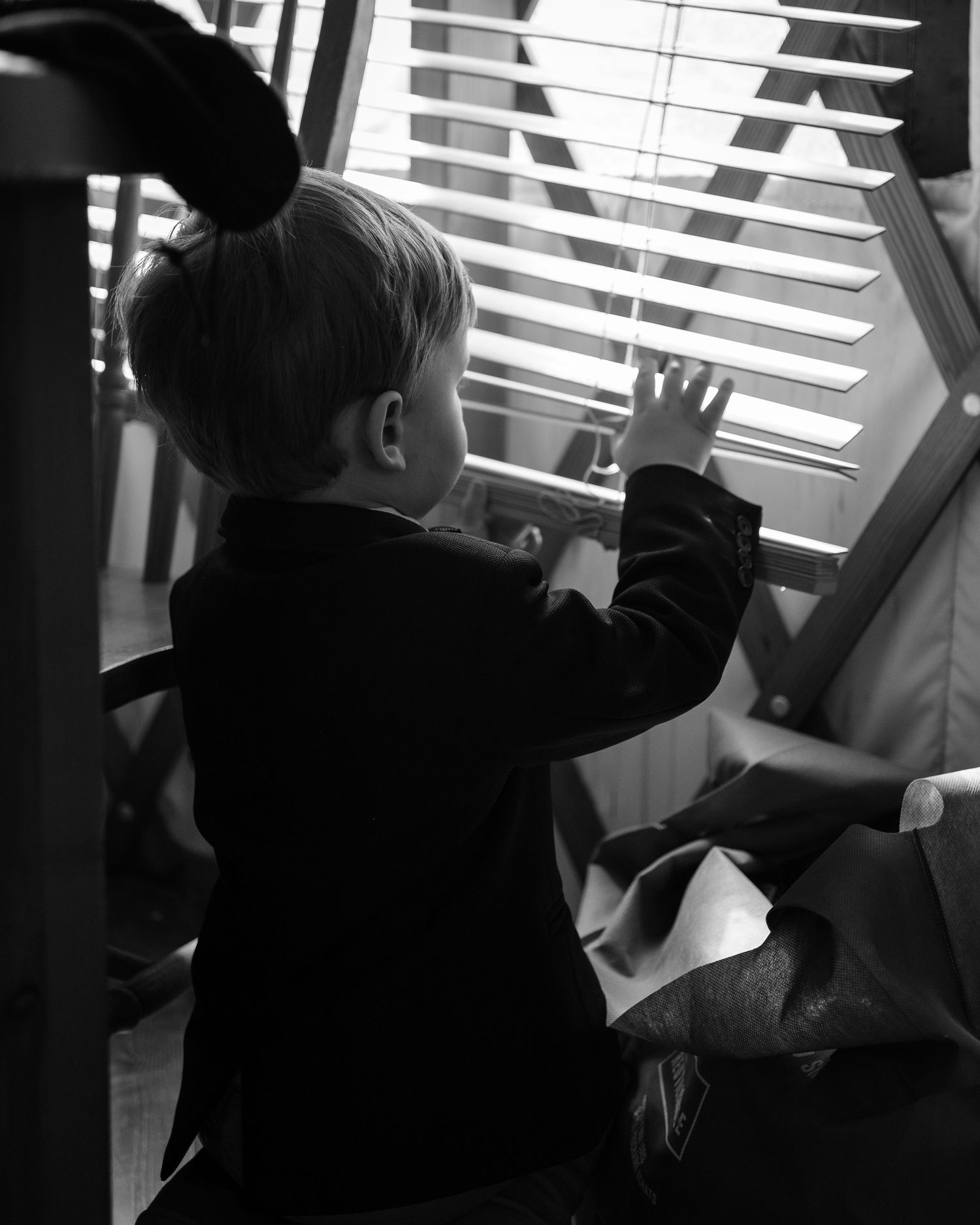 Candid black and white shot of young wedding guest looking through window blinds