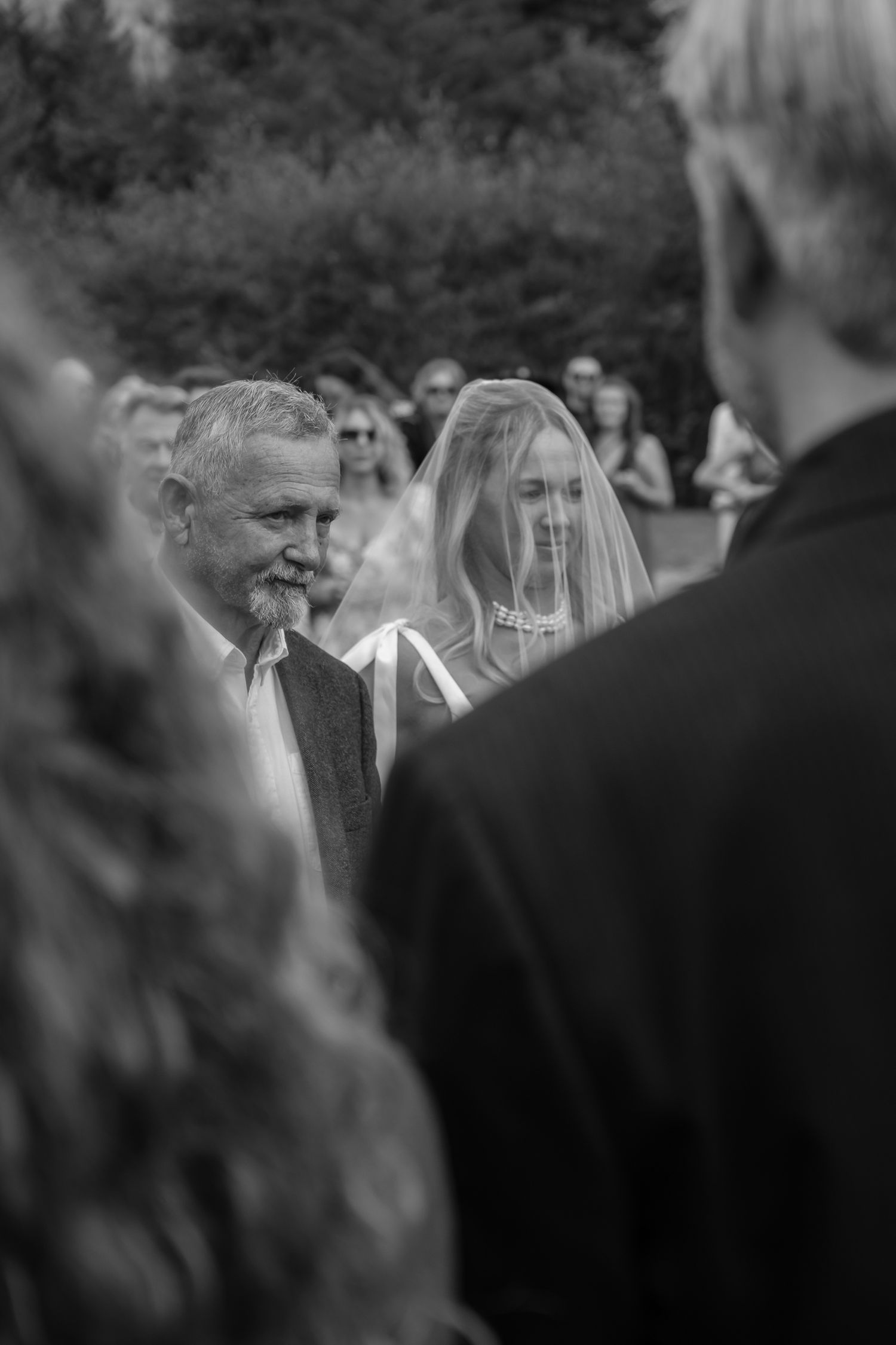 Black and white documentary shot of bride walking down aisle past smiling guests
