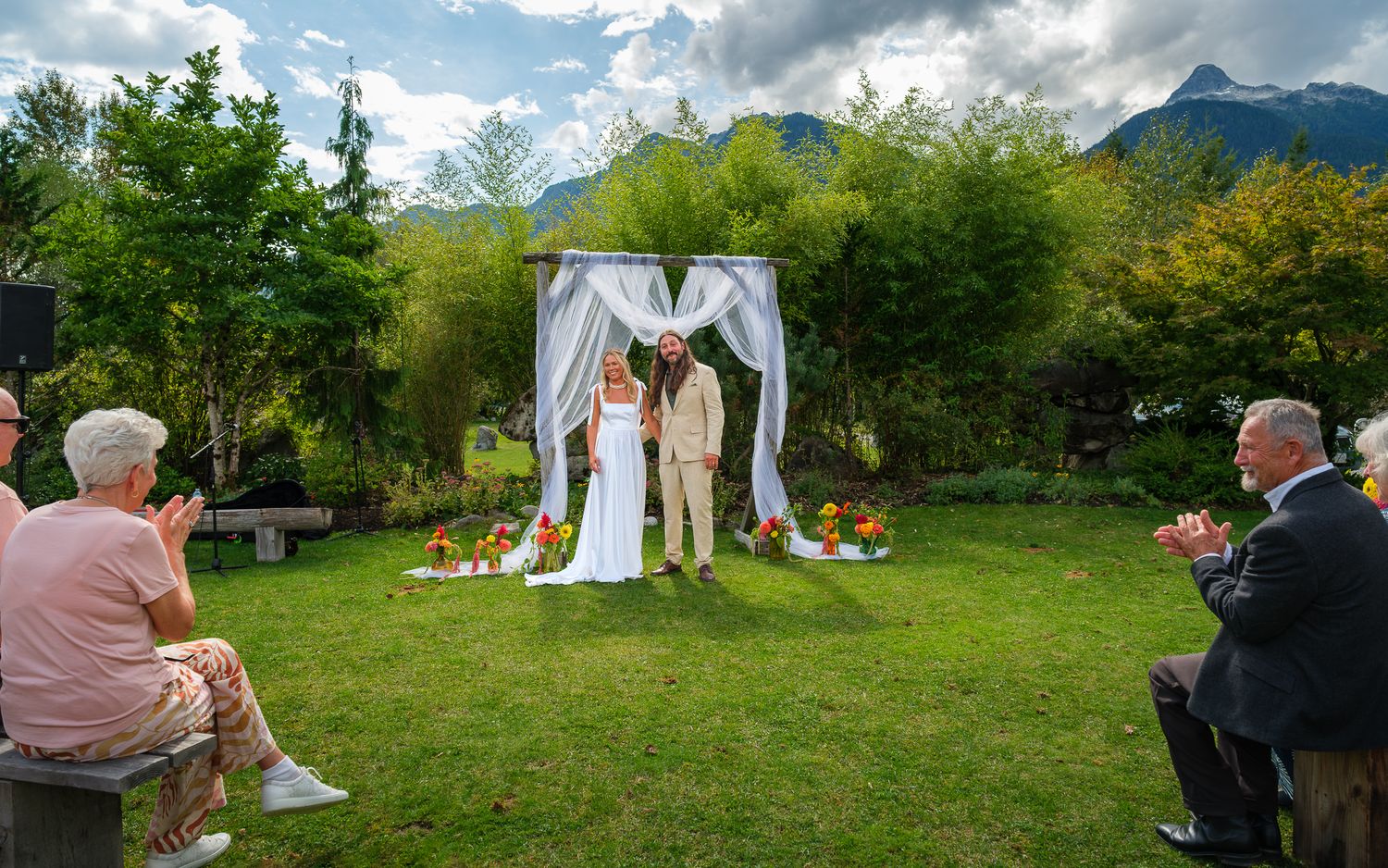 Wide outdoor wedding ceremony shot with couple at floral arch and seated guests