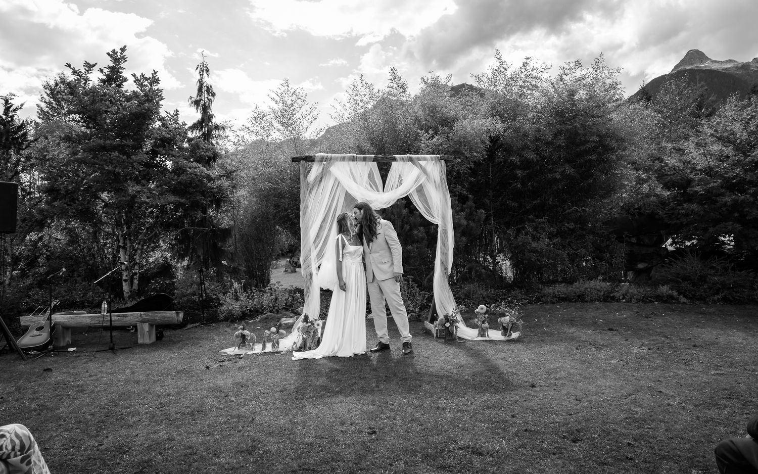 Black and white wedding photo of couple first kiss under ceremony arch