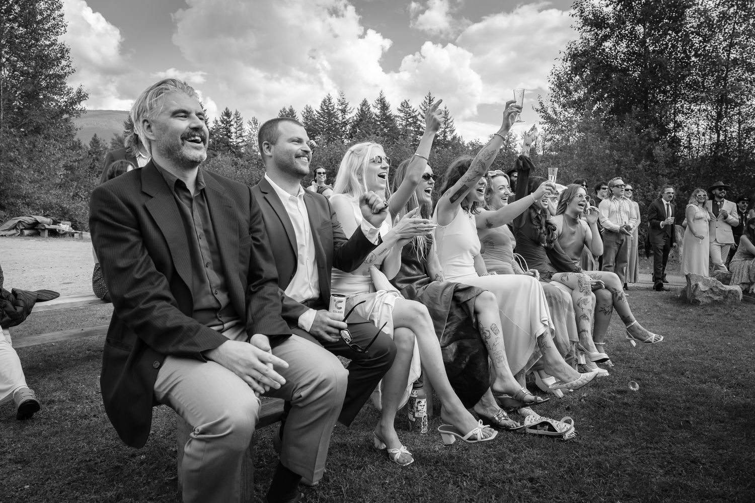Candid black and white shot of wedding guests cheering during outdoor ceremony