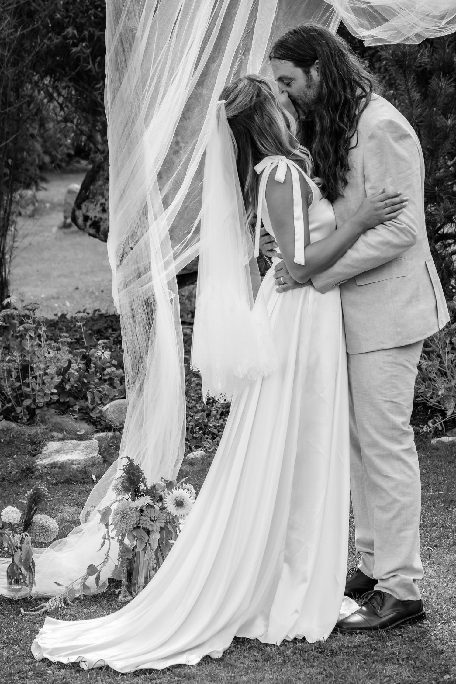 Black and white wedding photo of couple first kiss under ceremony arch