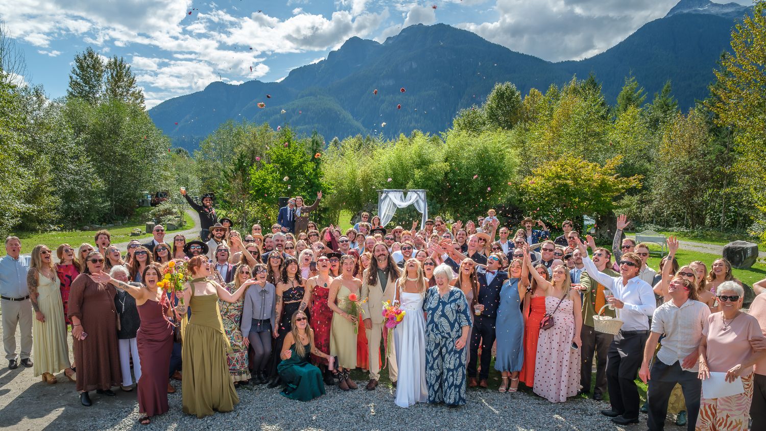 Candid wedding group photo with guests celebrating outdoors under scenic mountains