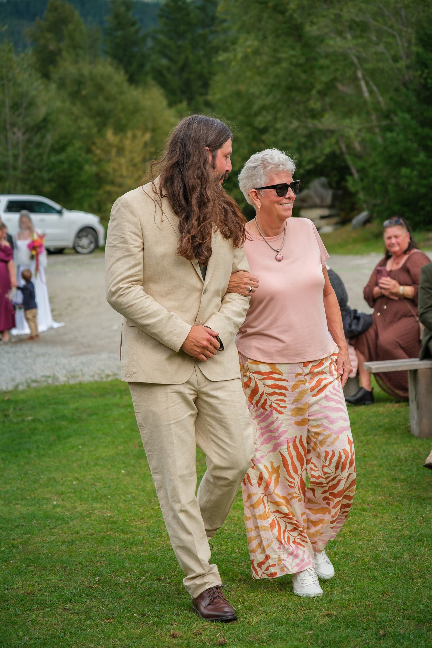 Candid wedding photo of groom walking down the aisle with his mother outdoors