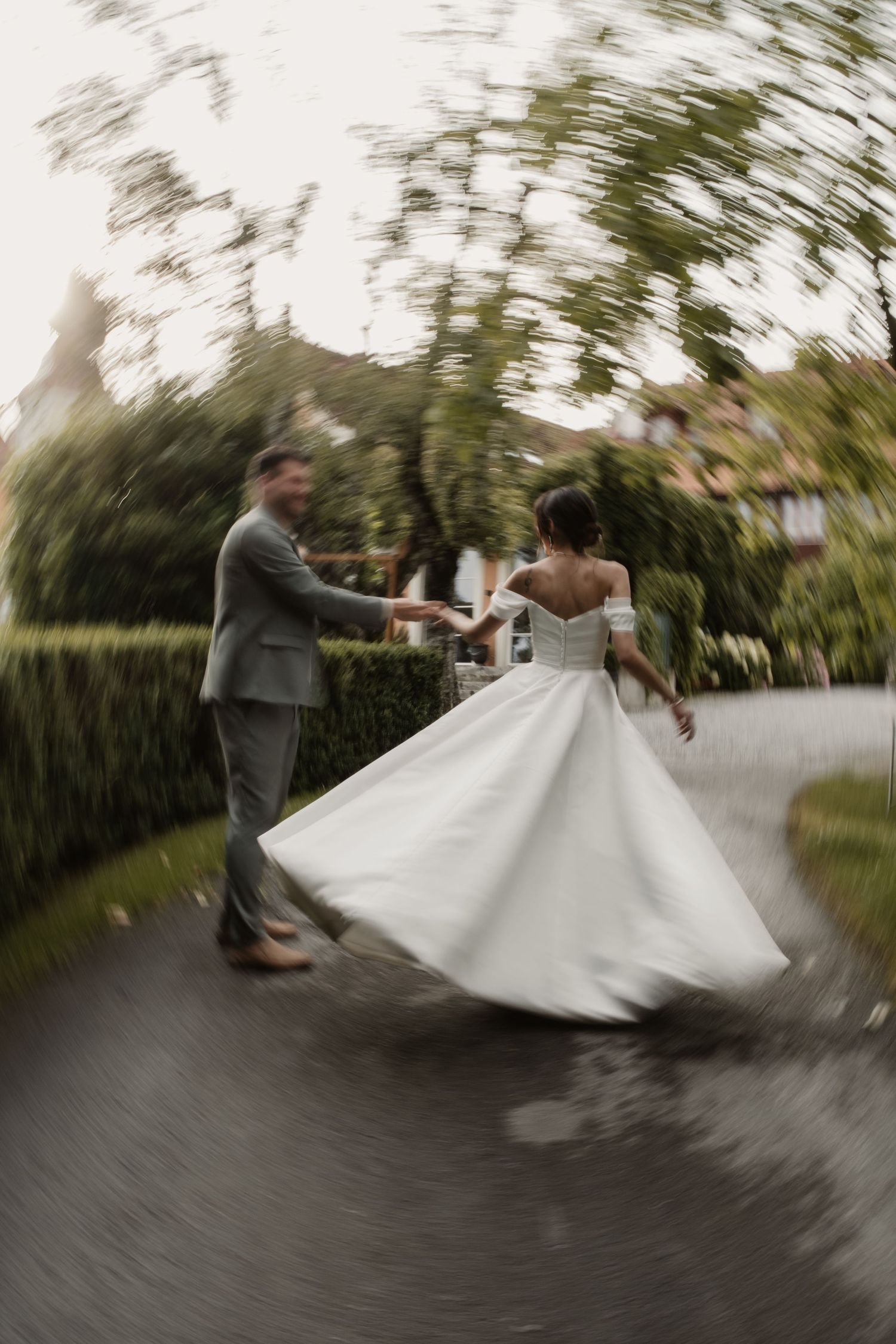 Bride in off-shoulder gown twirls with groom in artistic motion-blur wedding photo outdoors.