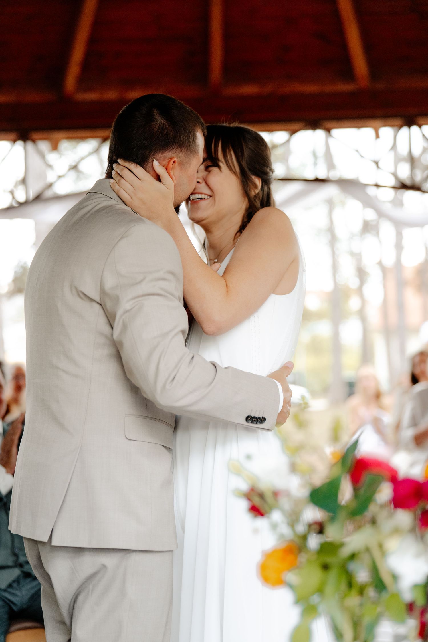 Laughing bride in white dress embraces groom in beige suit during first dance at wedding.
