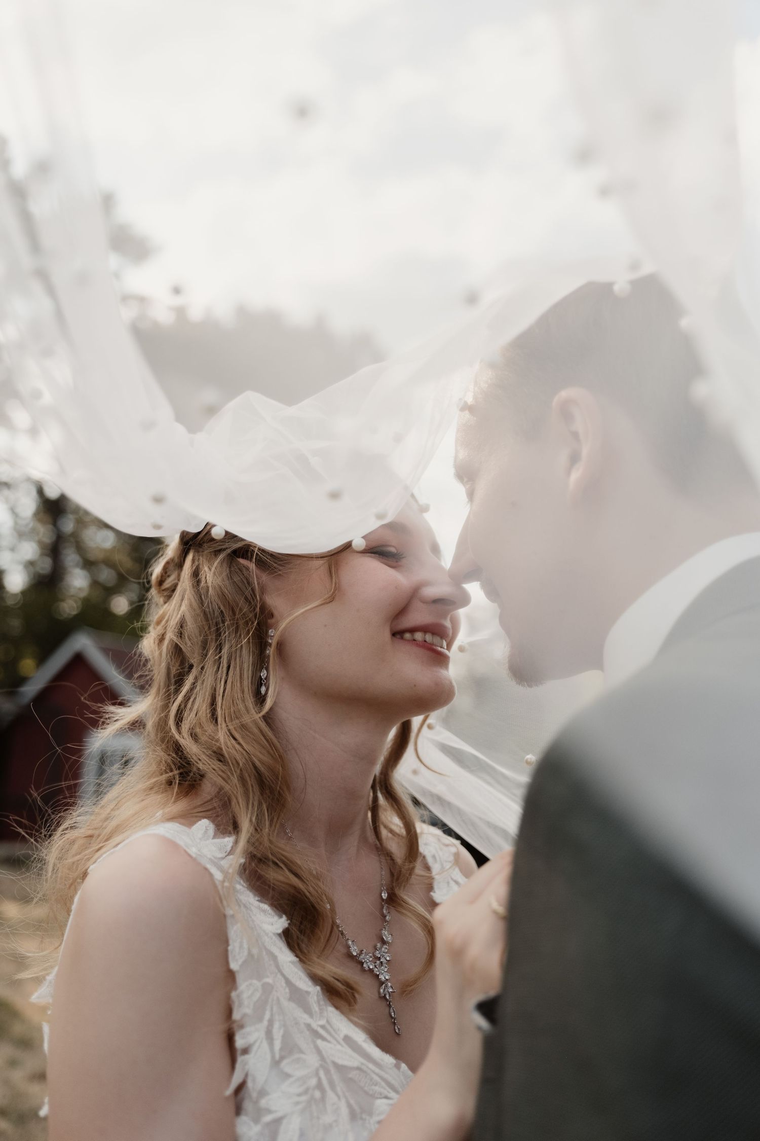Romantic bride and groom share intimate moment under flowing wedding veil outdoors.