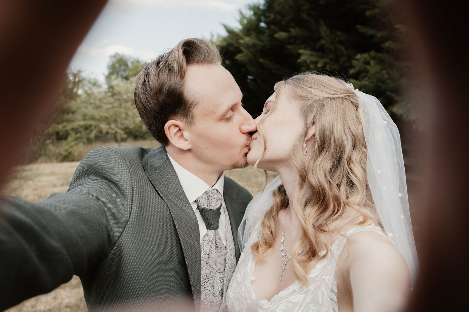 Bride and groom share a romantic kiss in a charming outdoor selfie portrait.