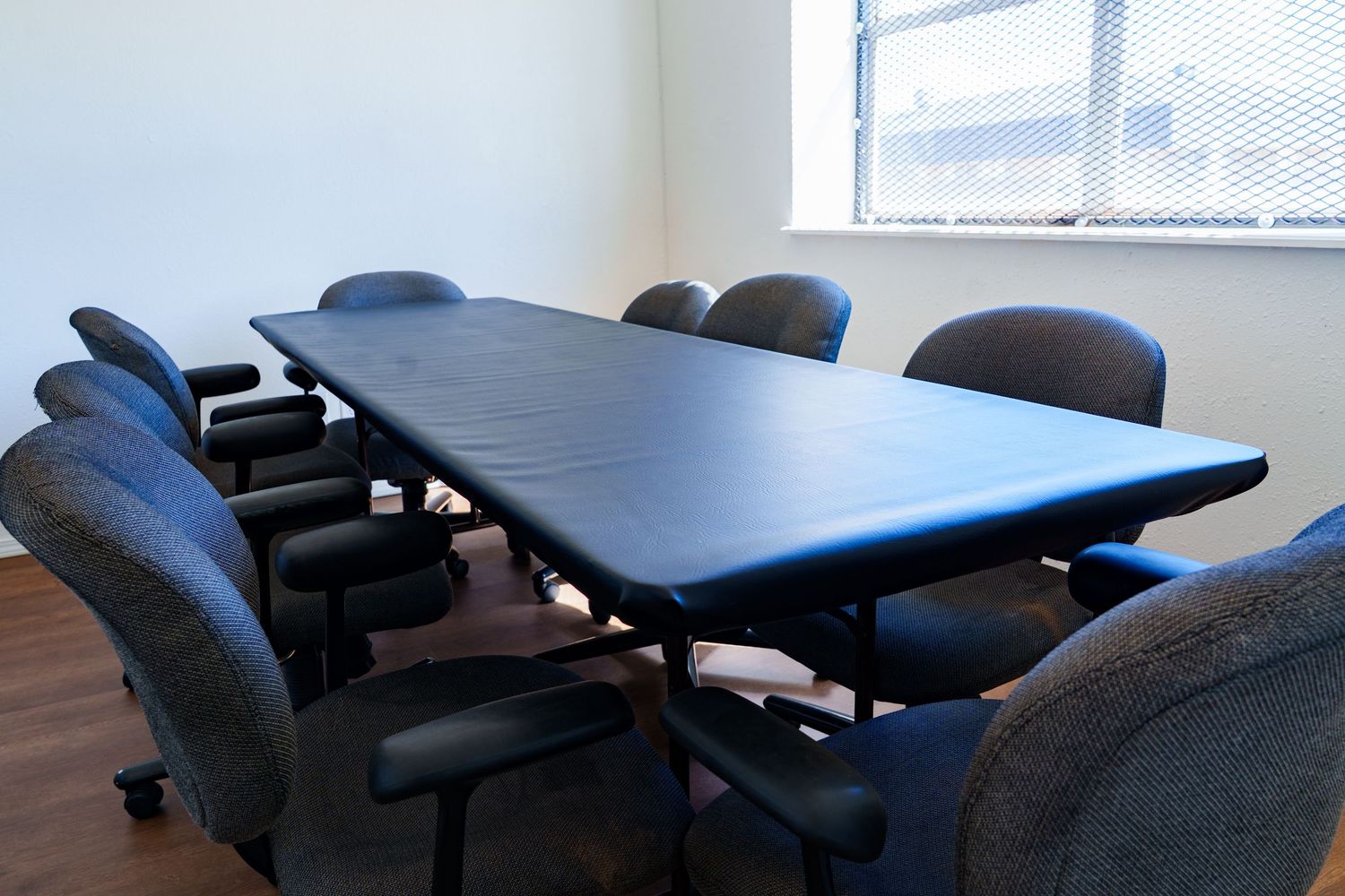 Modern conference room with a large black table and eight cushioned office chairs near a bright window.