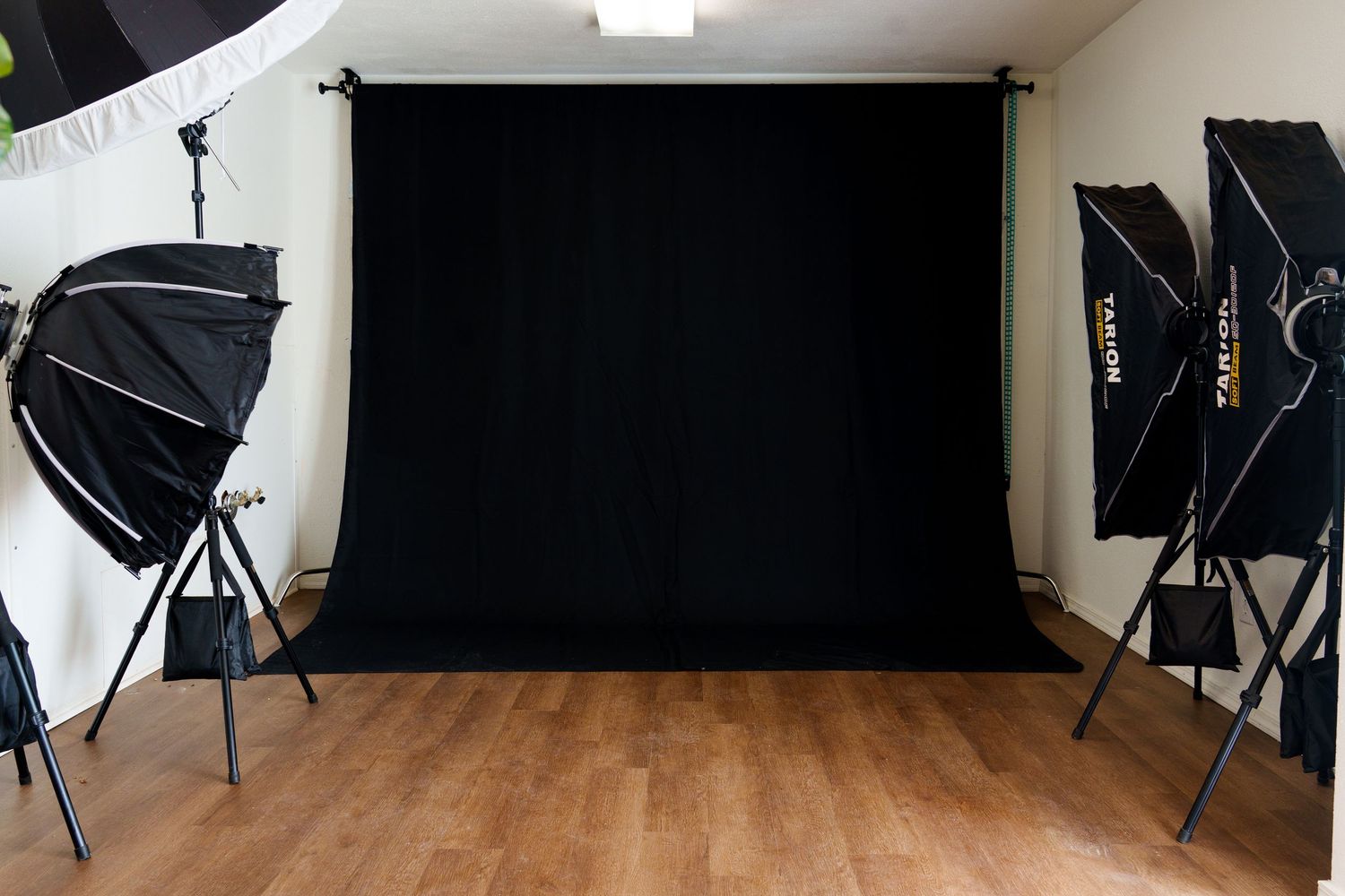 Professional photography studio with black backdrop, softbox lights, and hardwood floors ready for a photo shoot.