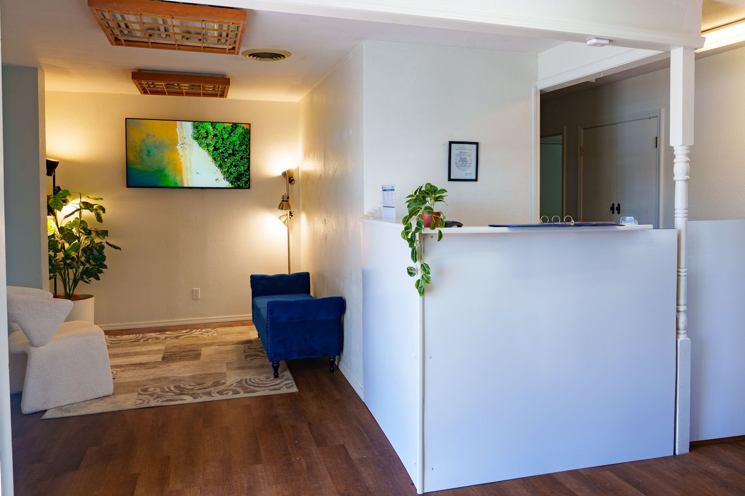 Modern reception area with white desk, blue accent chair, TV, and hardwood floors in a professional office.