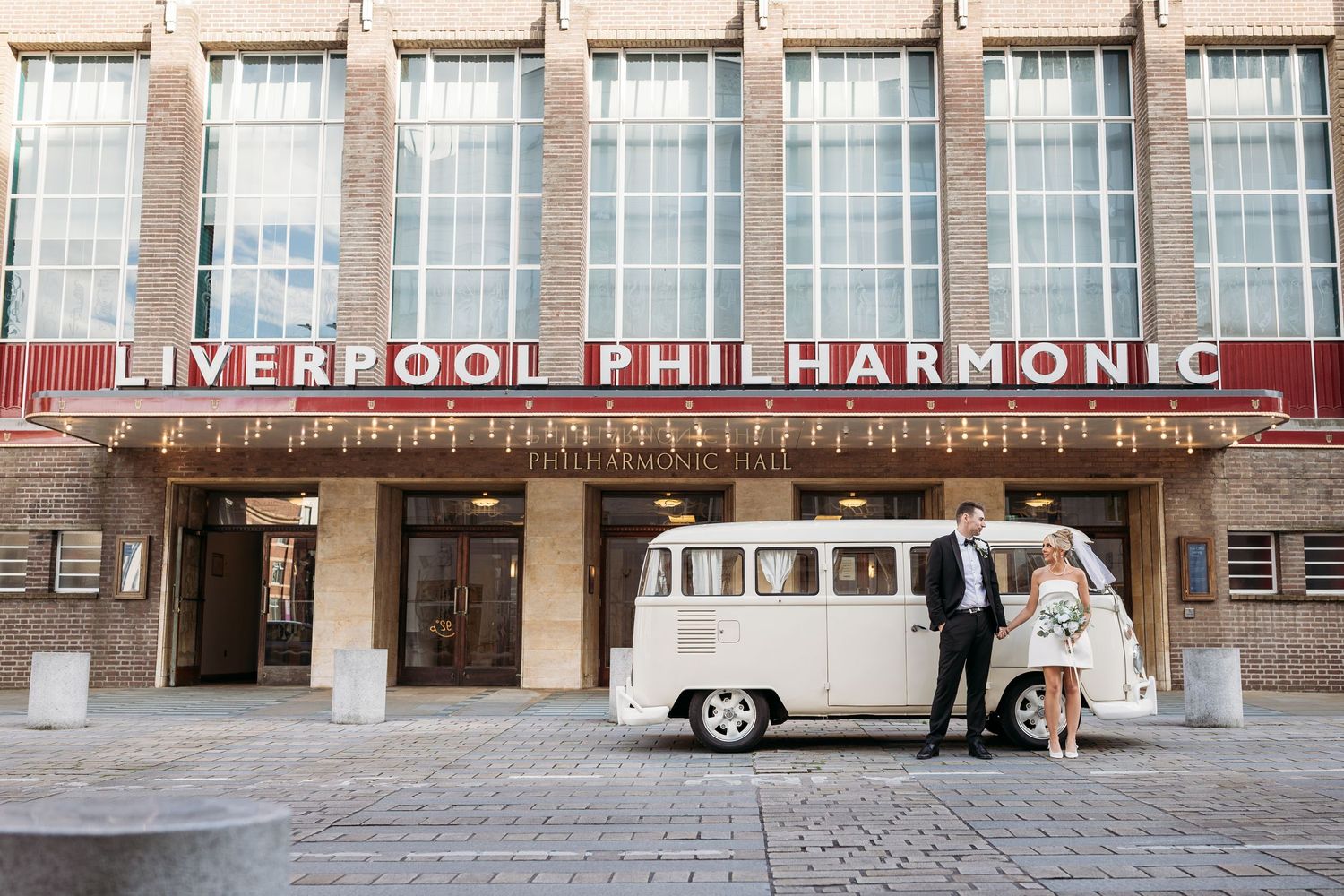 A newly married couple stand holding hands outside the Royal Philharmonic Hall, Liverpool.