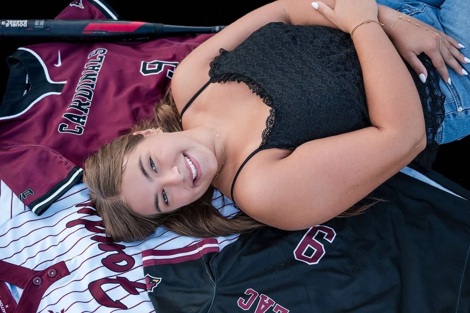 Young woman posing with Cardinals baseball jerseys, smiling while lying on sports uniforms outdoors.