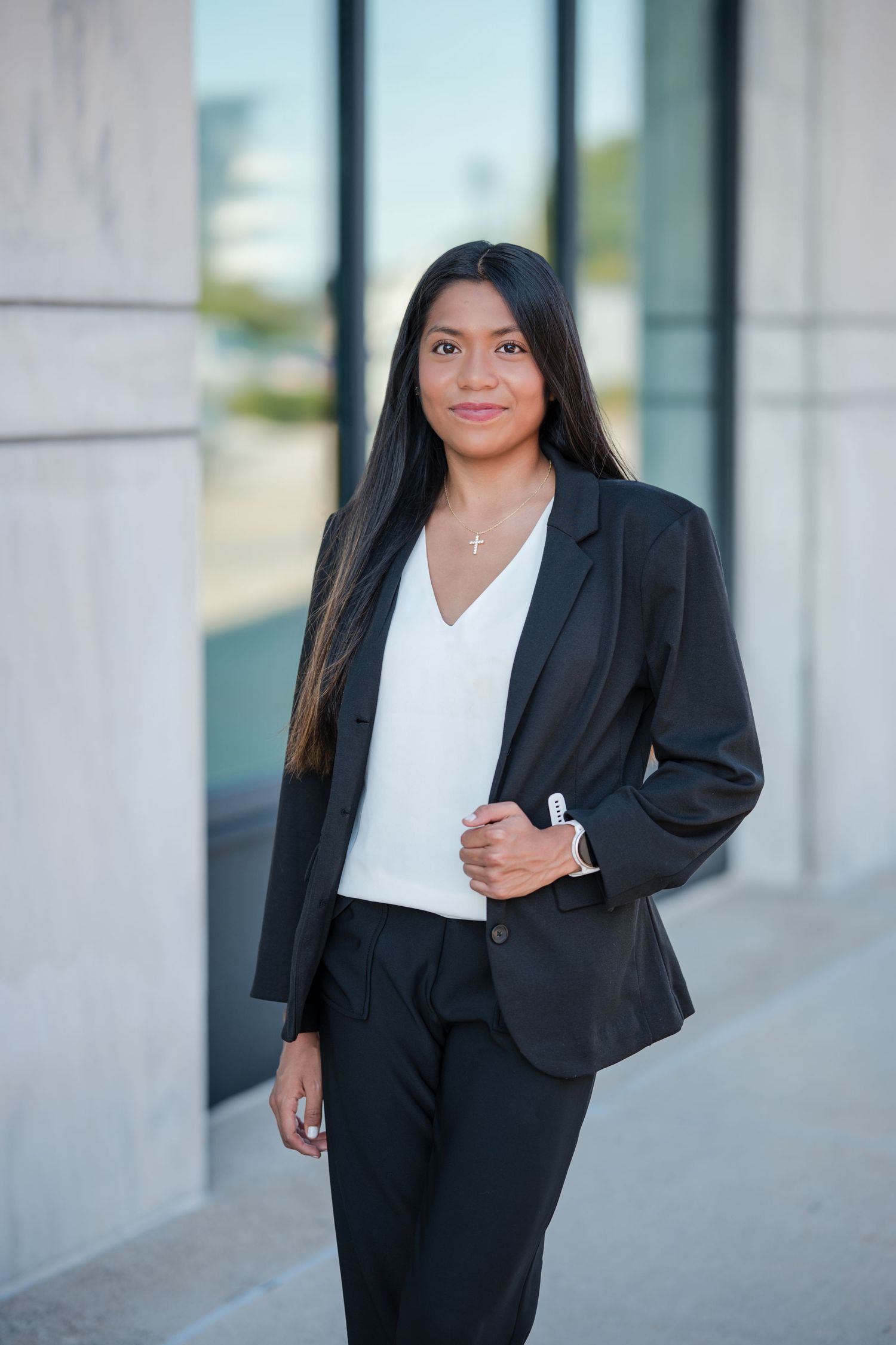 Professional woman in black suit and white blouse standing confidently outside a modern building.