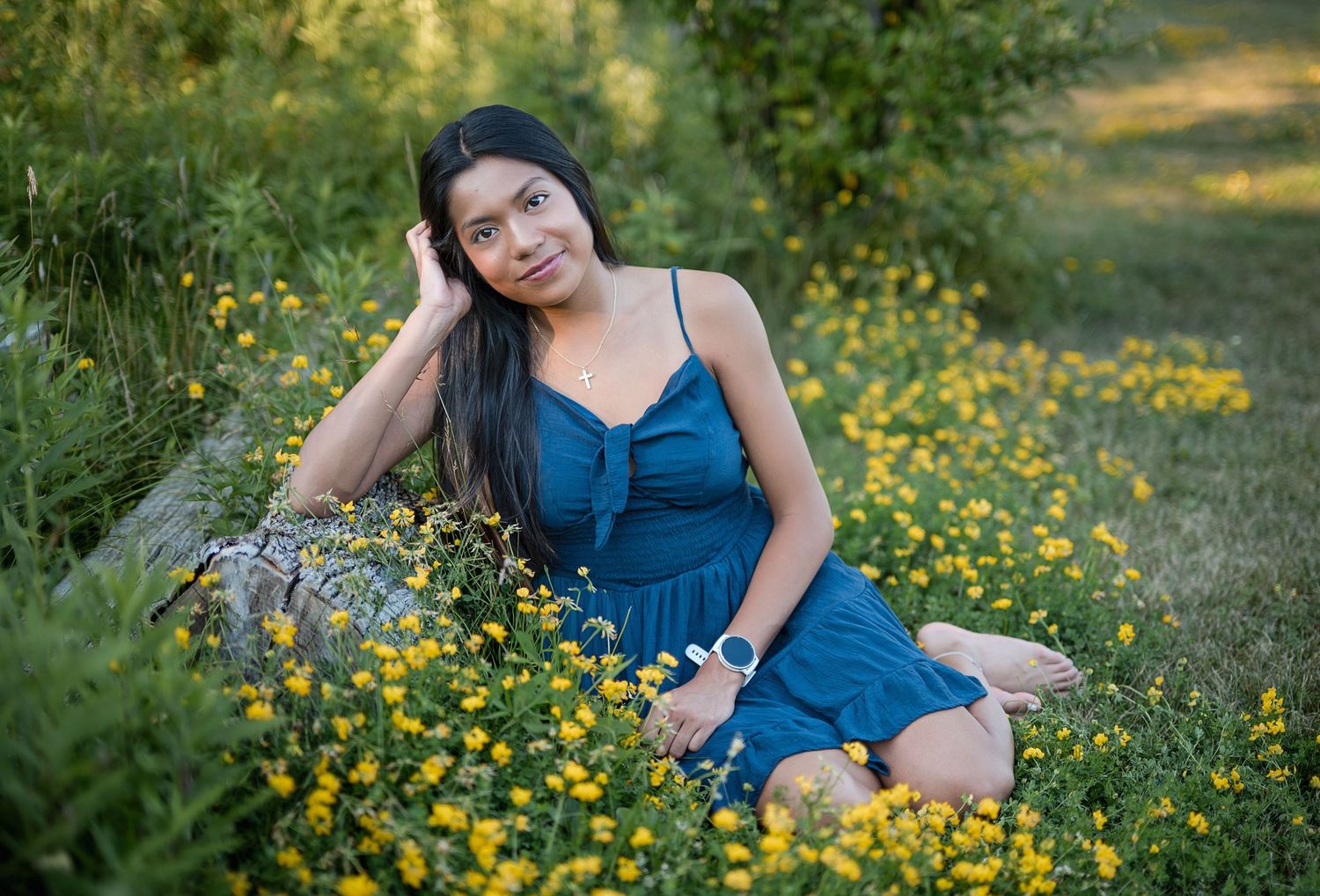 Young woman in blue dress sitting among yellow wildflowers and green grass in a serene outdoor garden setting.