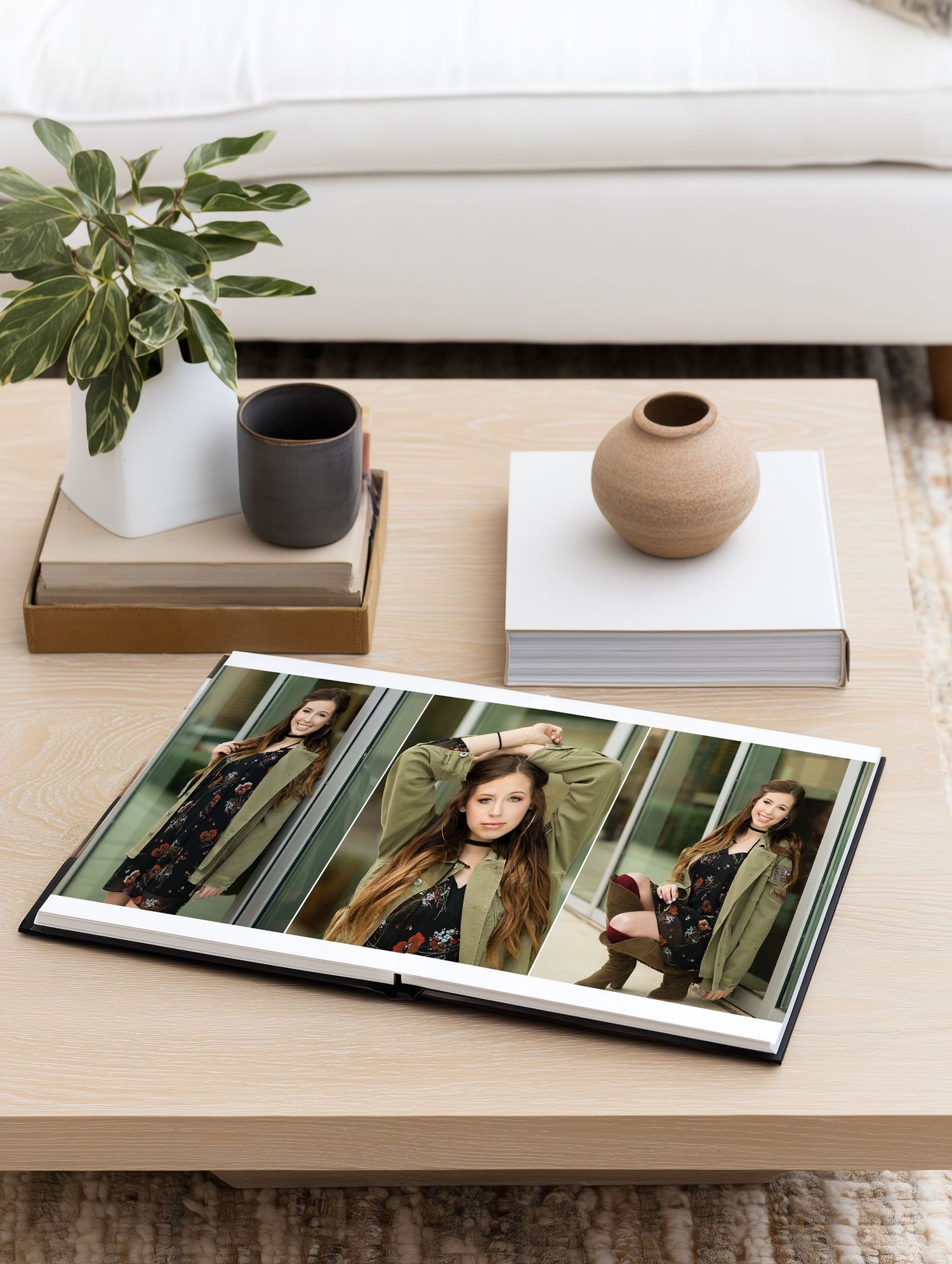 Open photo album on a light wood coffee table showing senior portraits of a young woman in a green jacket.
