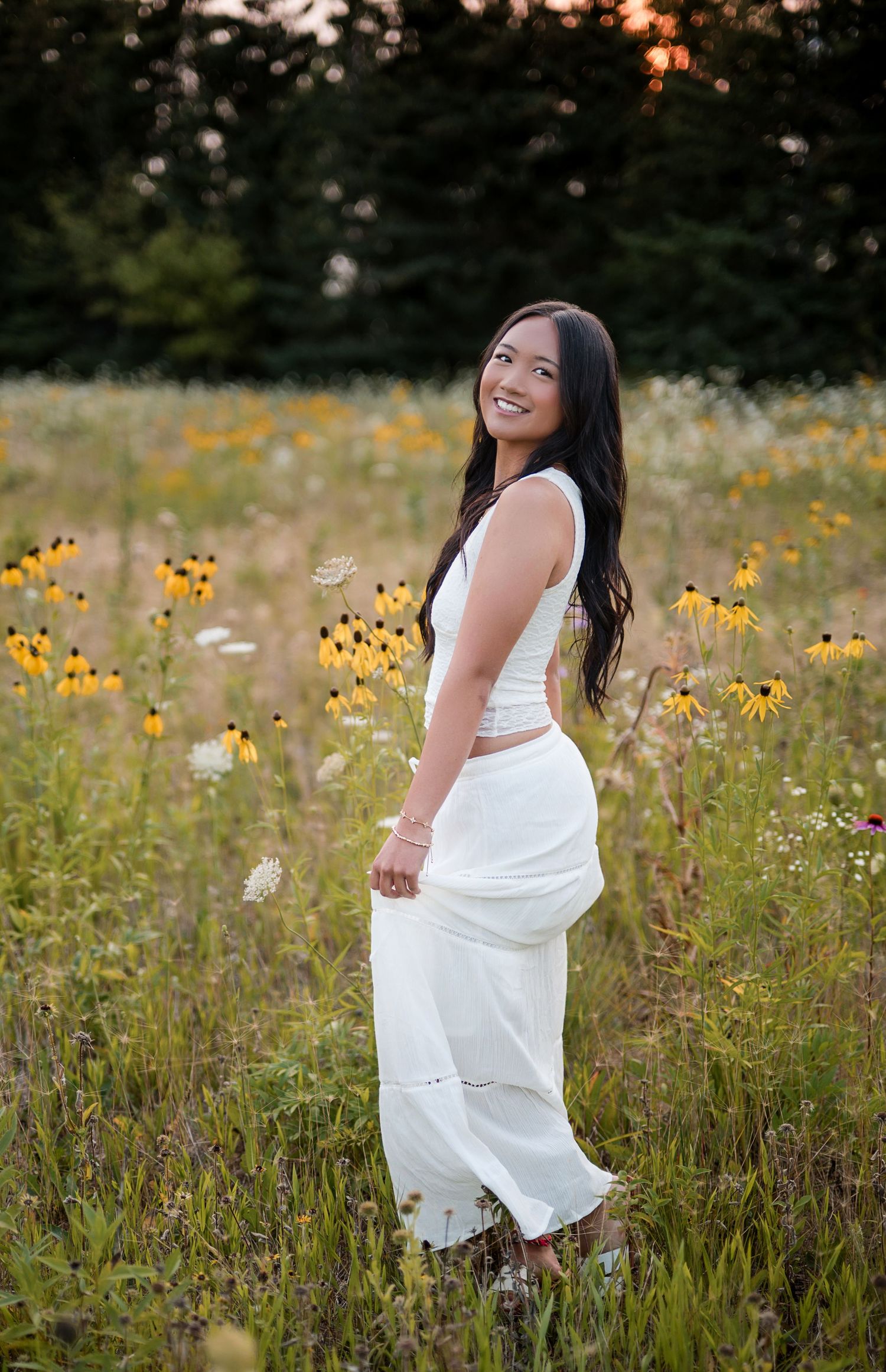 Young woman in white outfit smiling in a wildflower field with black-eyed Susans at golden hour.