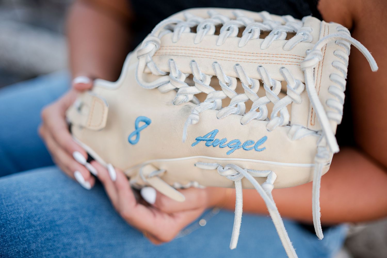 Close-up of a white baseball glove personalized with the name Angel and number 8 in blue lettering.