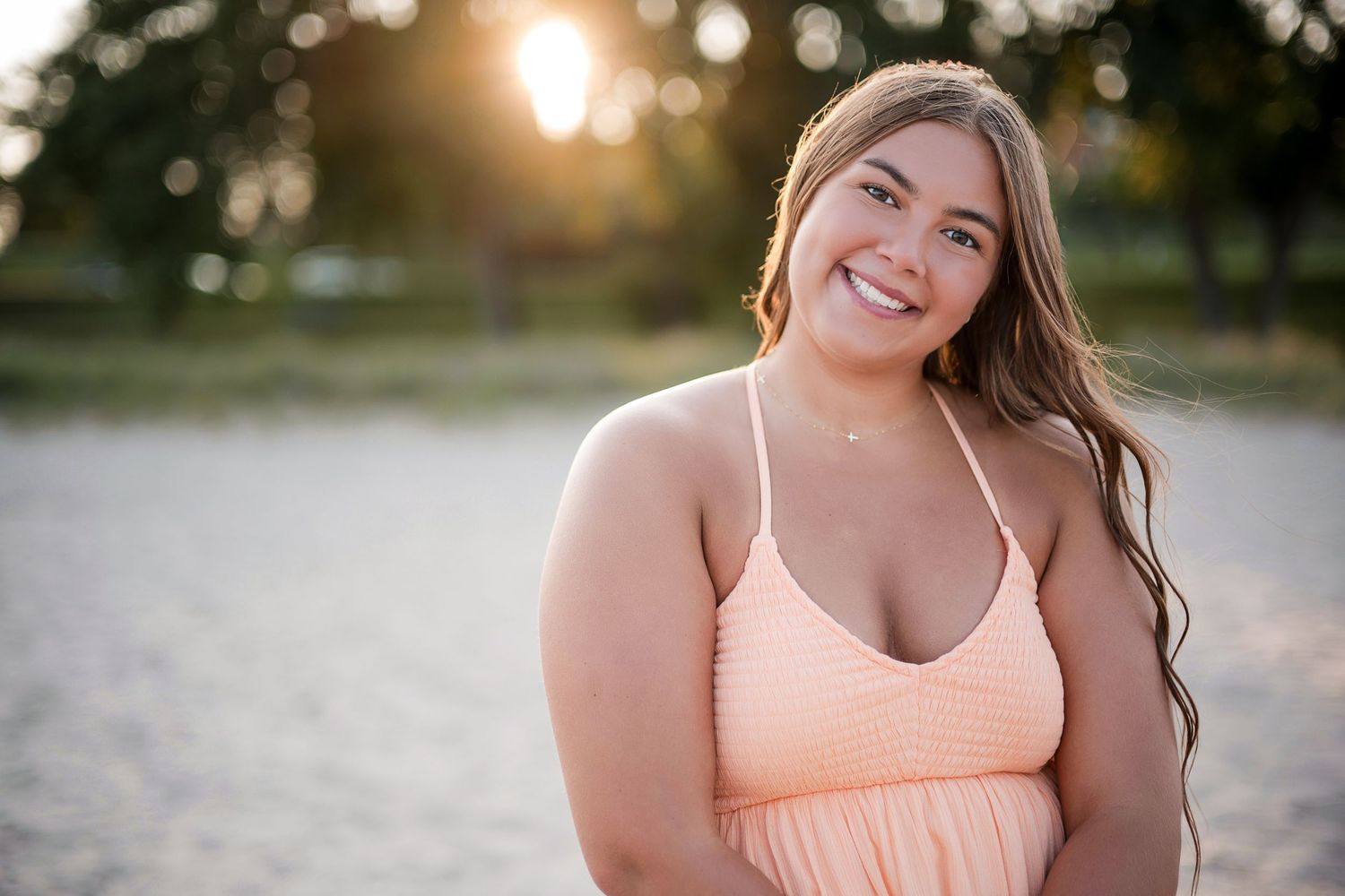 Smiling young woman in peach sundress posing on sandy beach at golden hour sunset.